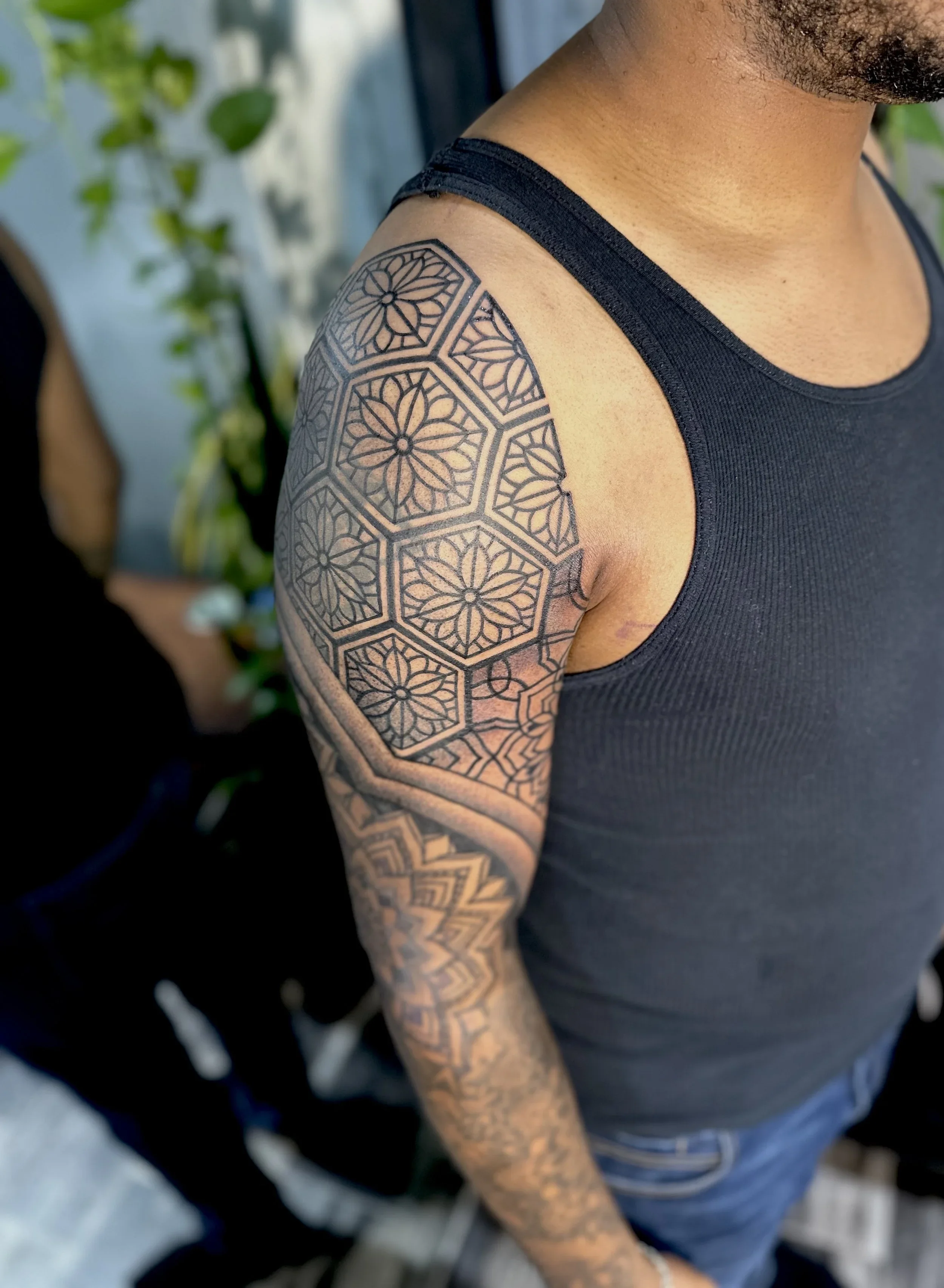 A close-up of a man's shoulder and arm, showcasing an intricate black geometric tattoo design on his upper arm.