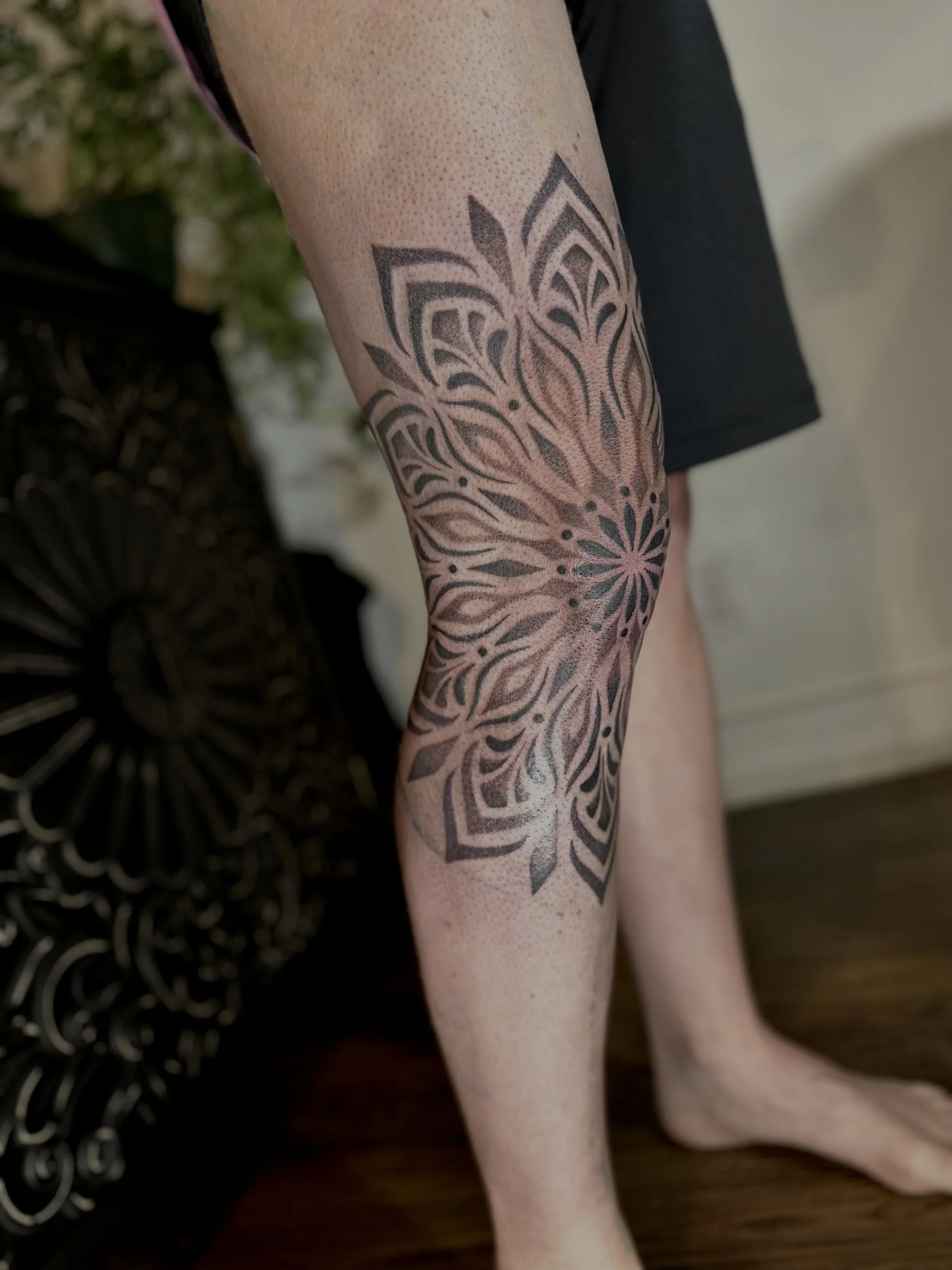 Close-up of a person's forearm with a black tattoo of a floral design.