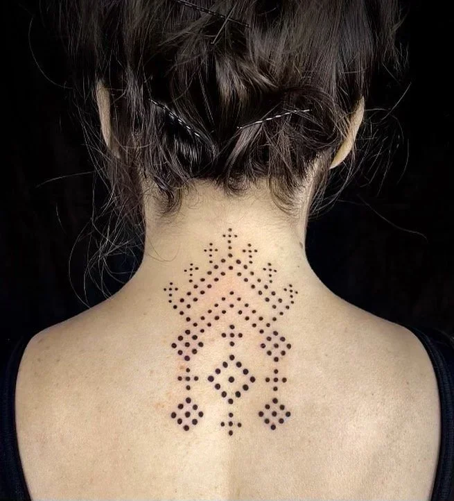 Back of a person's neck and shoulders with a tattoo of a geometric design composed of small black dots.