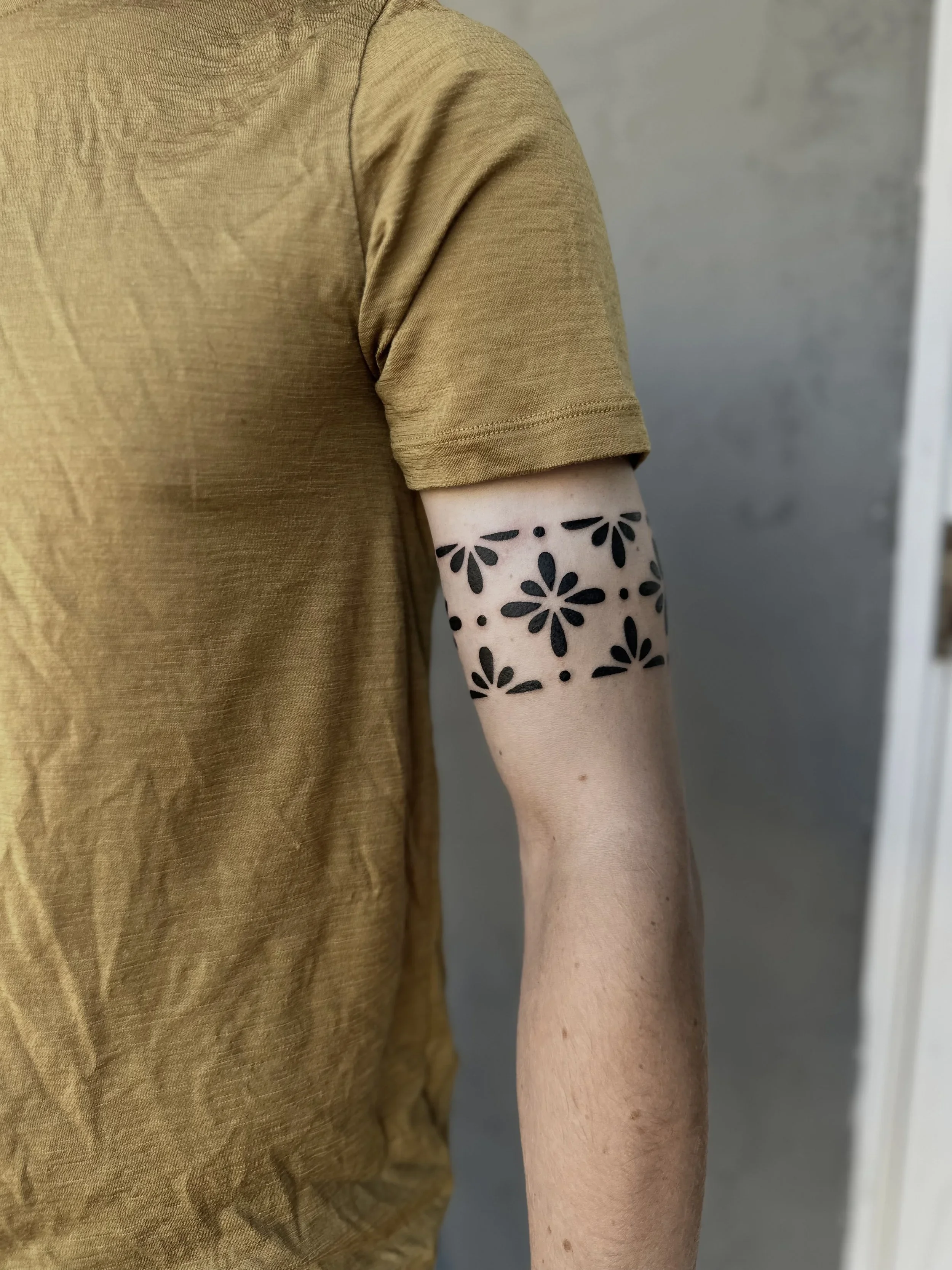 Person wearing a mustard yellow T-shirt with a floral tattoo on their forearm.