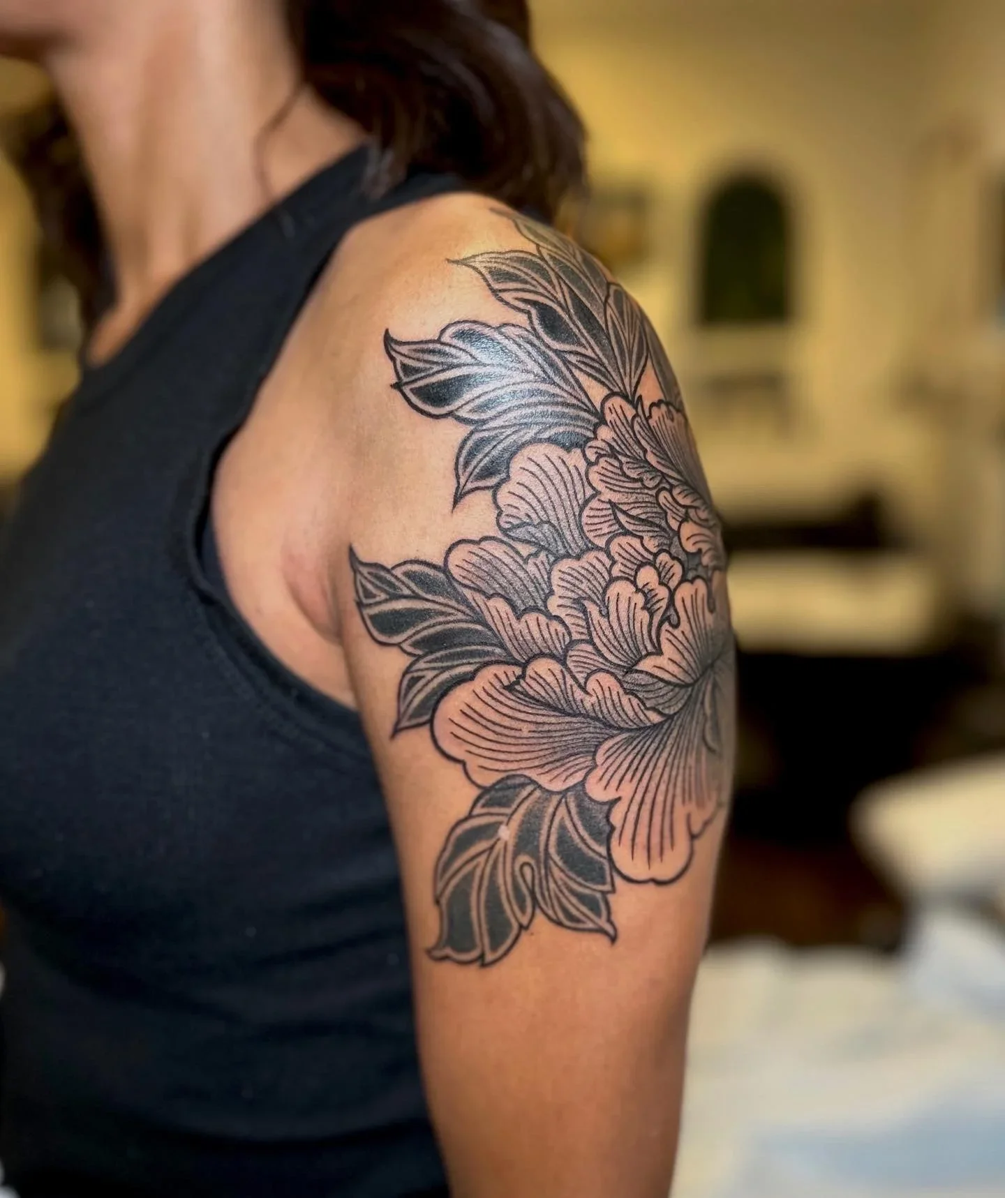 A close-up of a person's shoulder and upper arm, showcasing a large floral tattoo with bold outlines and intricate details.
