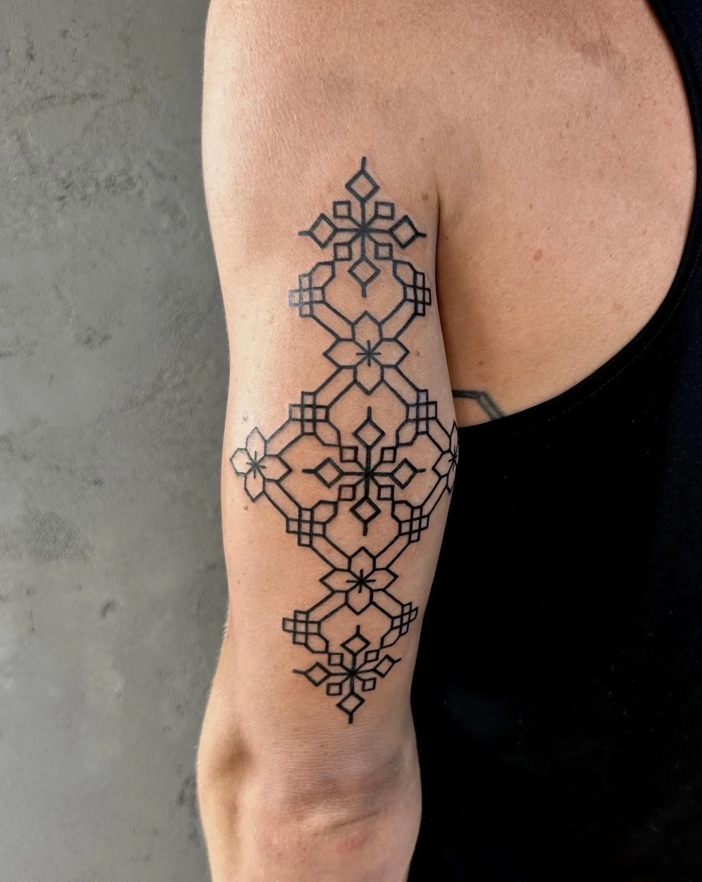 Black geometric tattoo on person's arm, extending from wrist to elbow, with intricate patterns and symmetrical shapes.