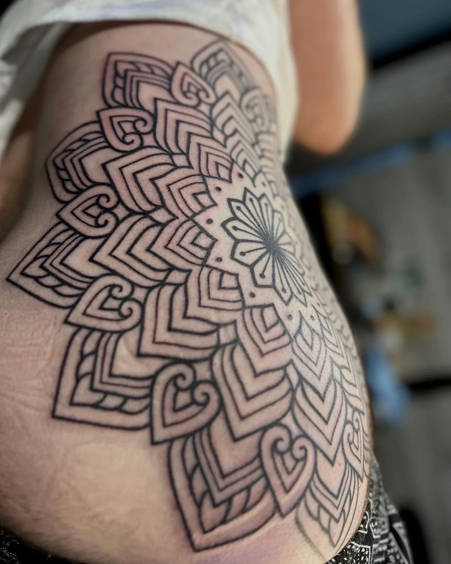 Line art tattoo of a symmetrical mandala design on a person's upper arm.
