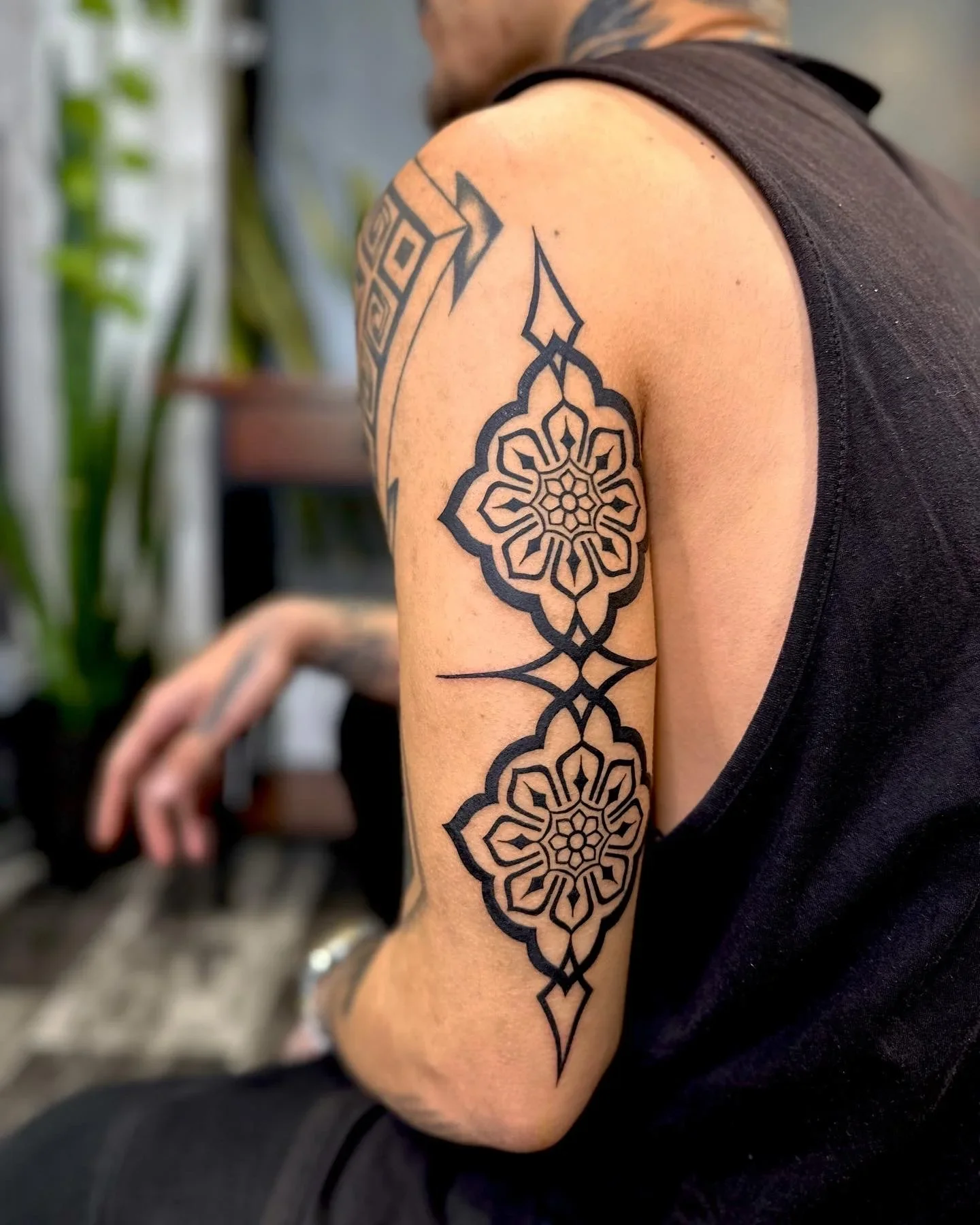 Close-up of a person's upper arm showing a large black geometric and floral tattoo design.