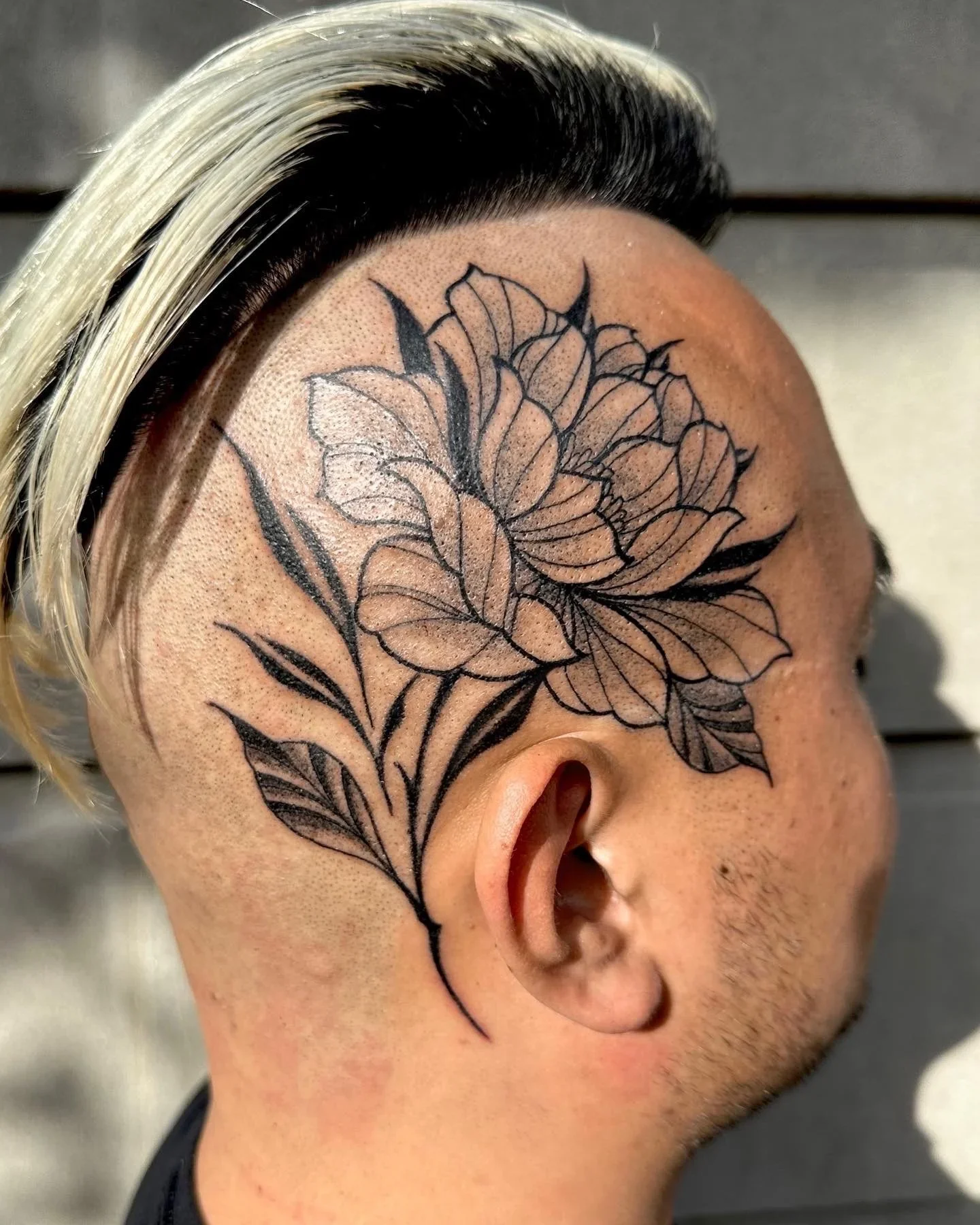 A person's head with a black and white hairstyle and a large floral tattoo on the side of the face and scalp.