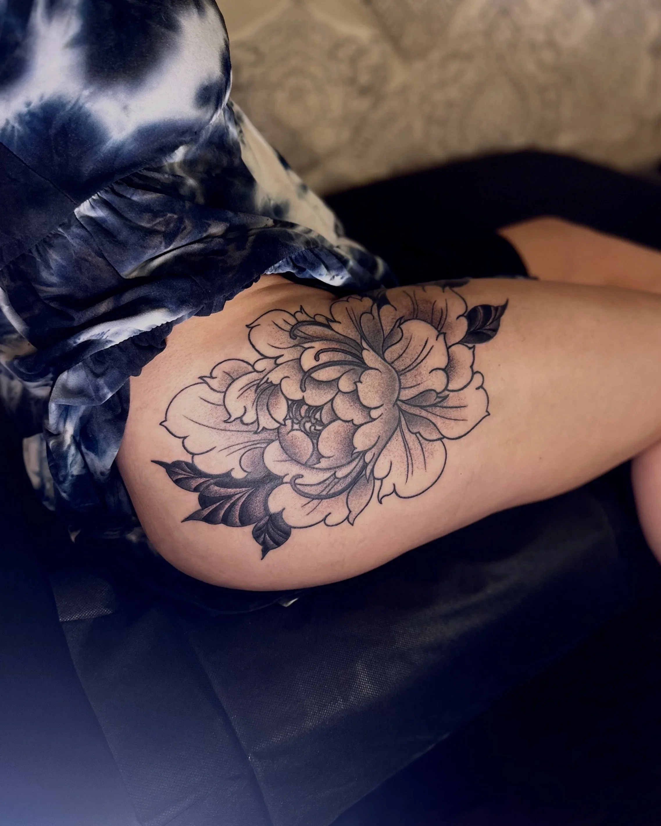 Close-up of a tattoo of a large floral design on a person's arm, with part of their clothing visible nearby.