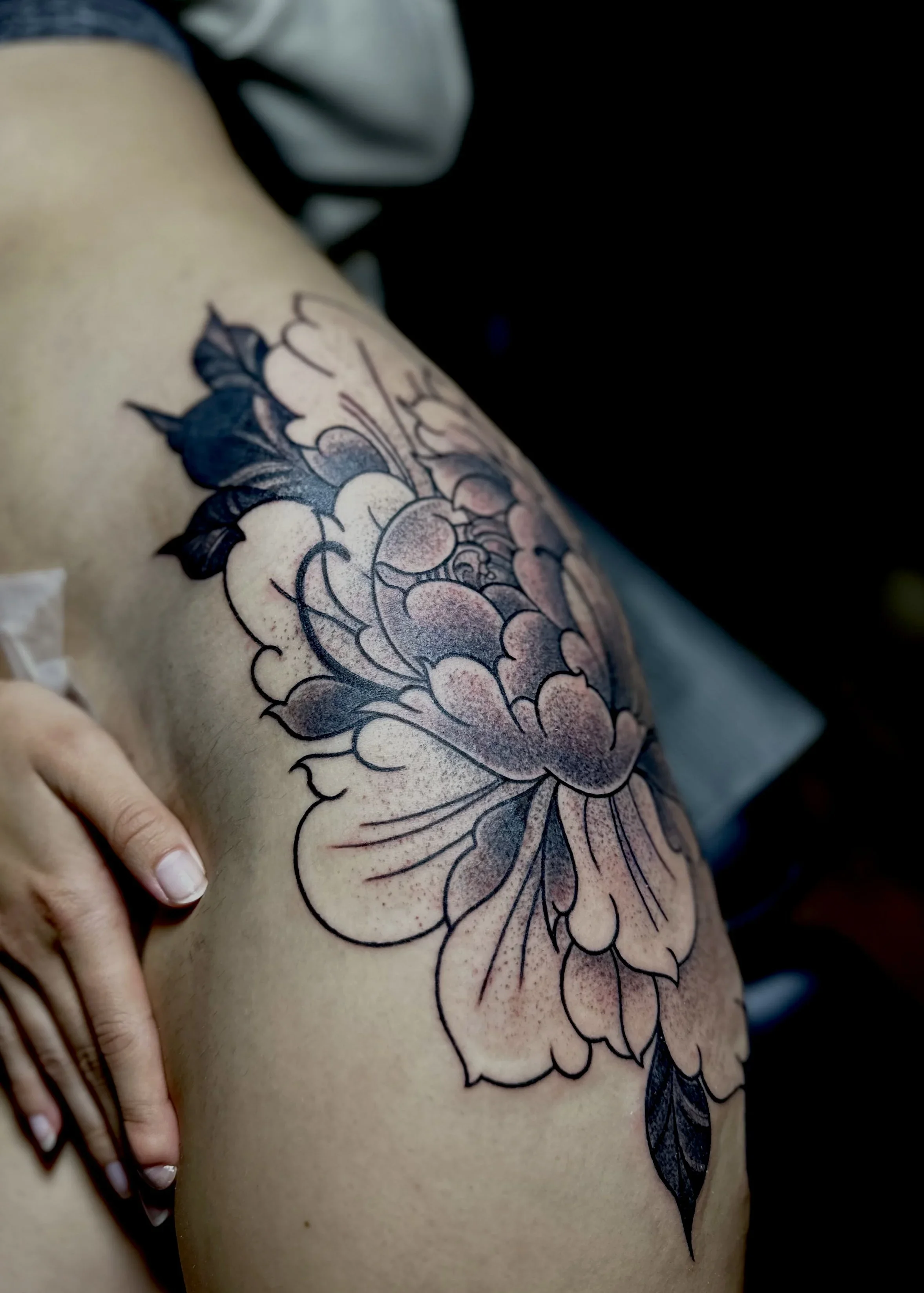 Tattoo of a floral design on a person's upper arm, featuring large outlined flowers with shading and leaves.