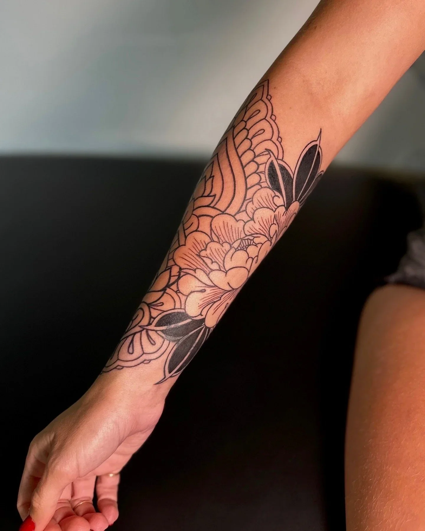 A person with a floral tattoo on their arm, resting their hand on a surface, with a dark background.