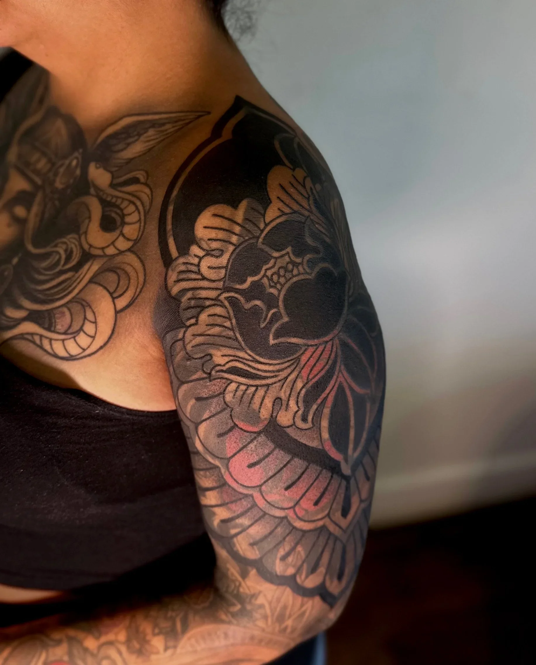 Close-up of a person's upper arm and shoulder with black and gray tribal-style tattoo artwork.