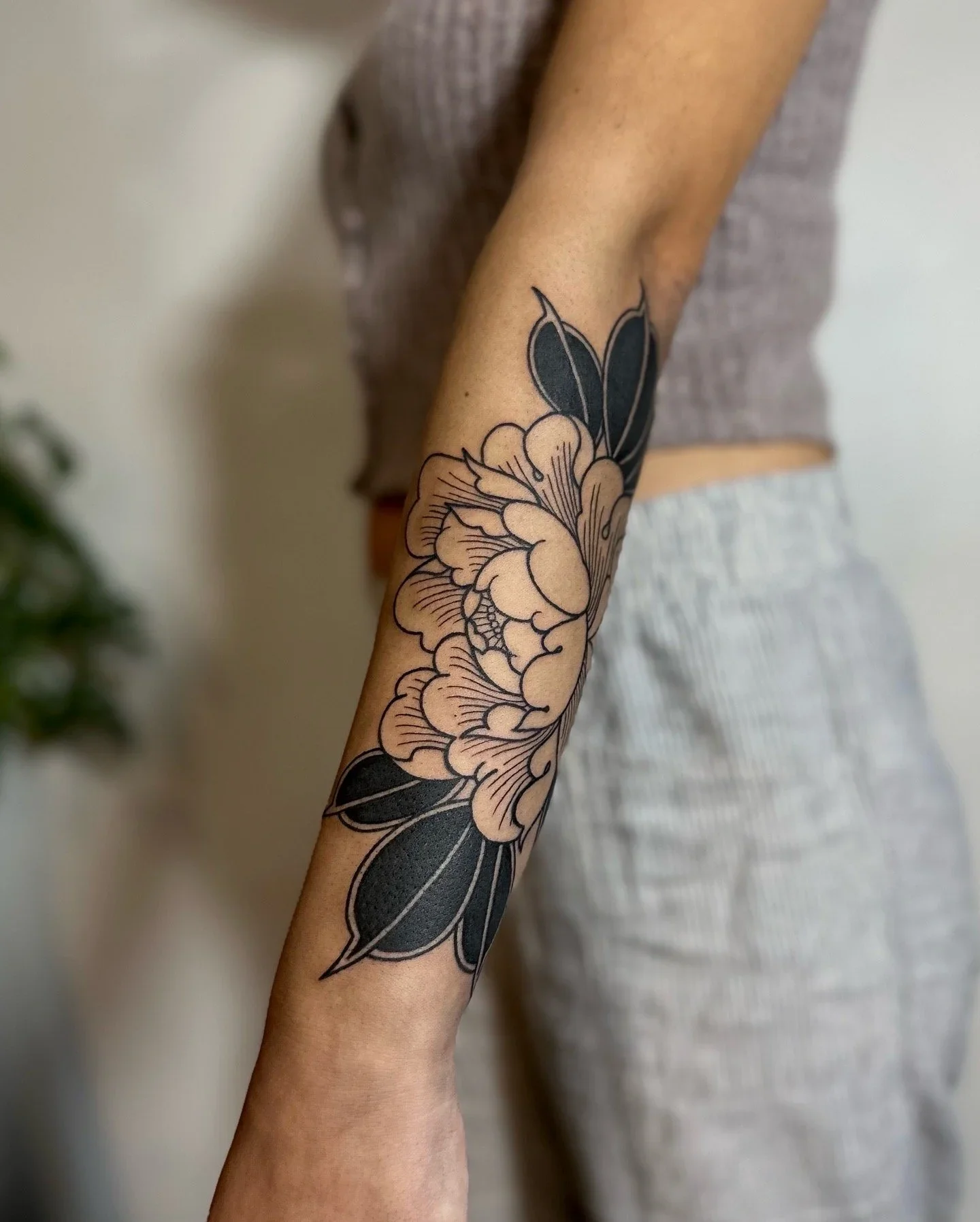 A person's arm with a large black and white floral tattoo featuring petals and leaves.