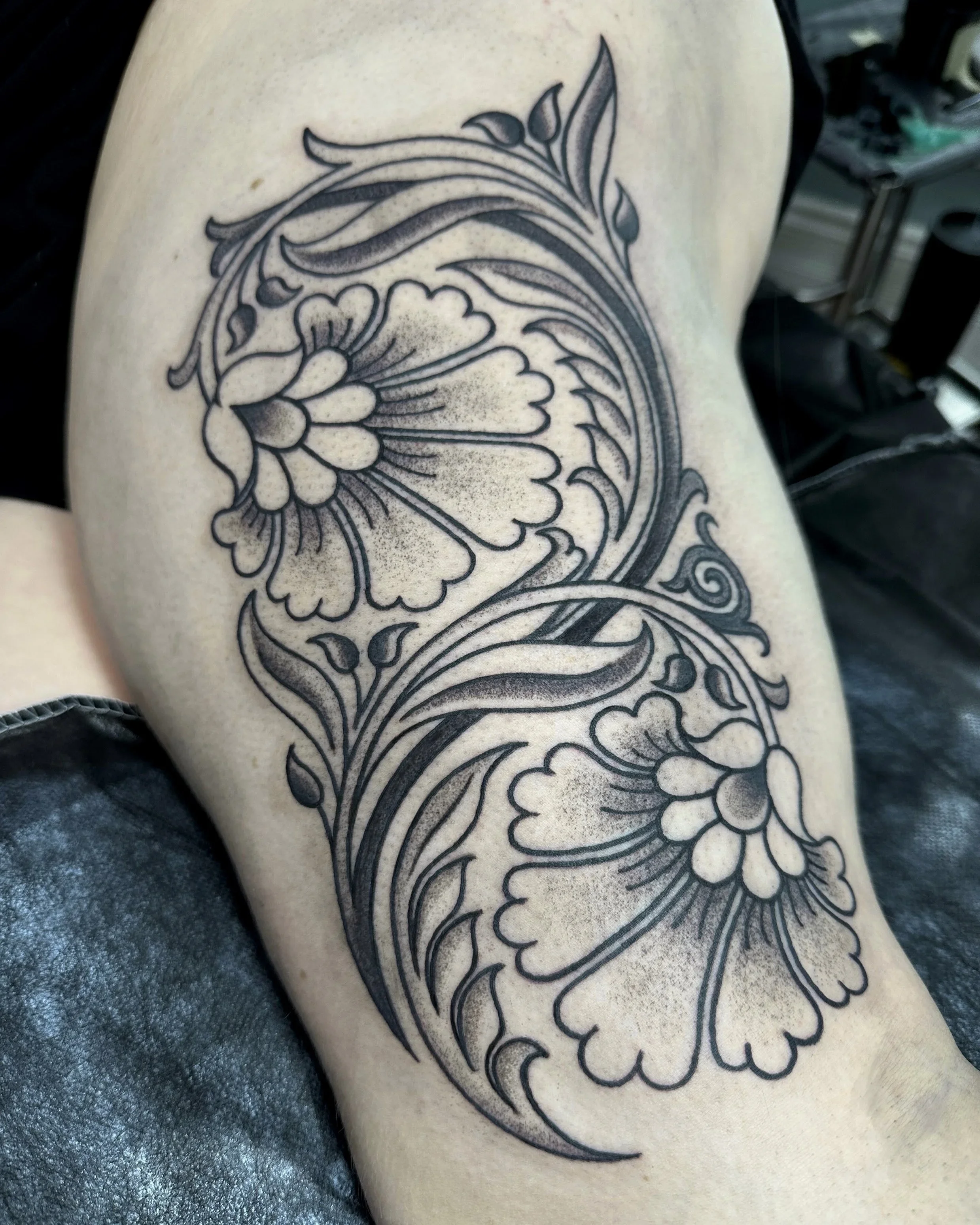 A black ink floral tattoo on a person's skin, featuring detailed line work and shading in a stylized design.
