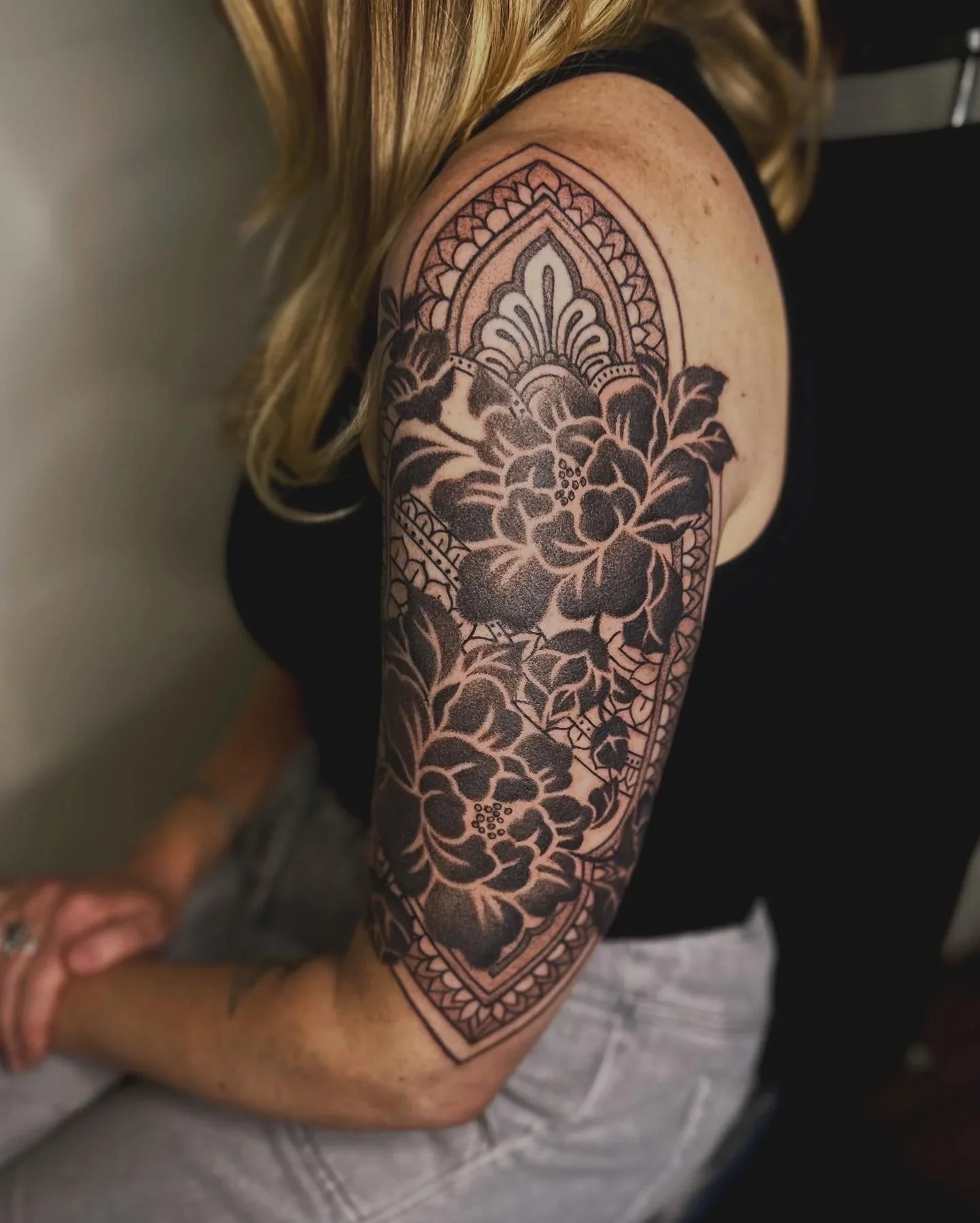 Black and gray floral tattoo with decorative patterns on a person's upper arm and shoulder.