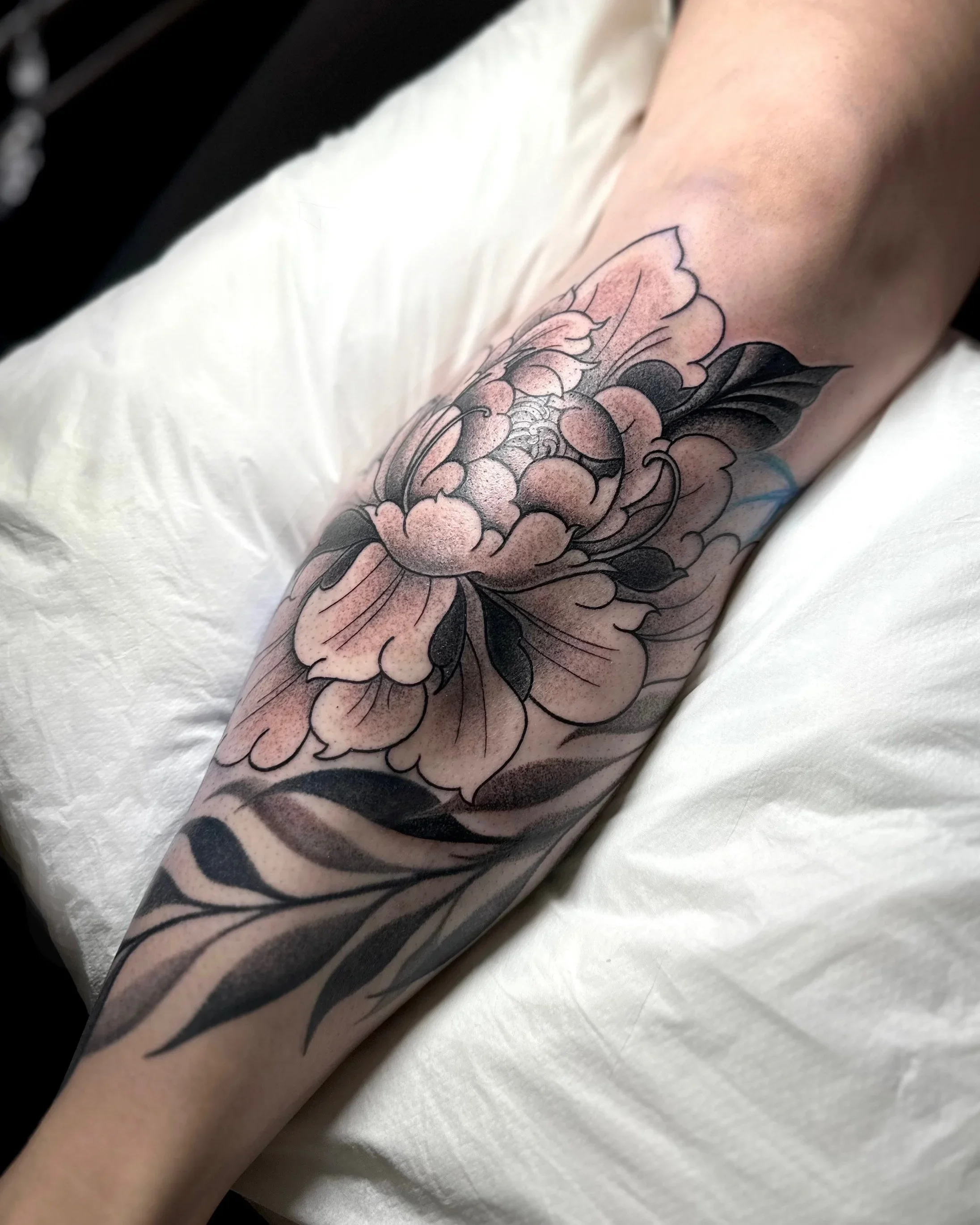 Close-up of a person's arm with a detailed tattoo of a flower with pink and black shading.