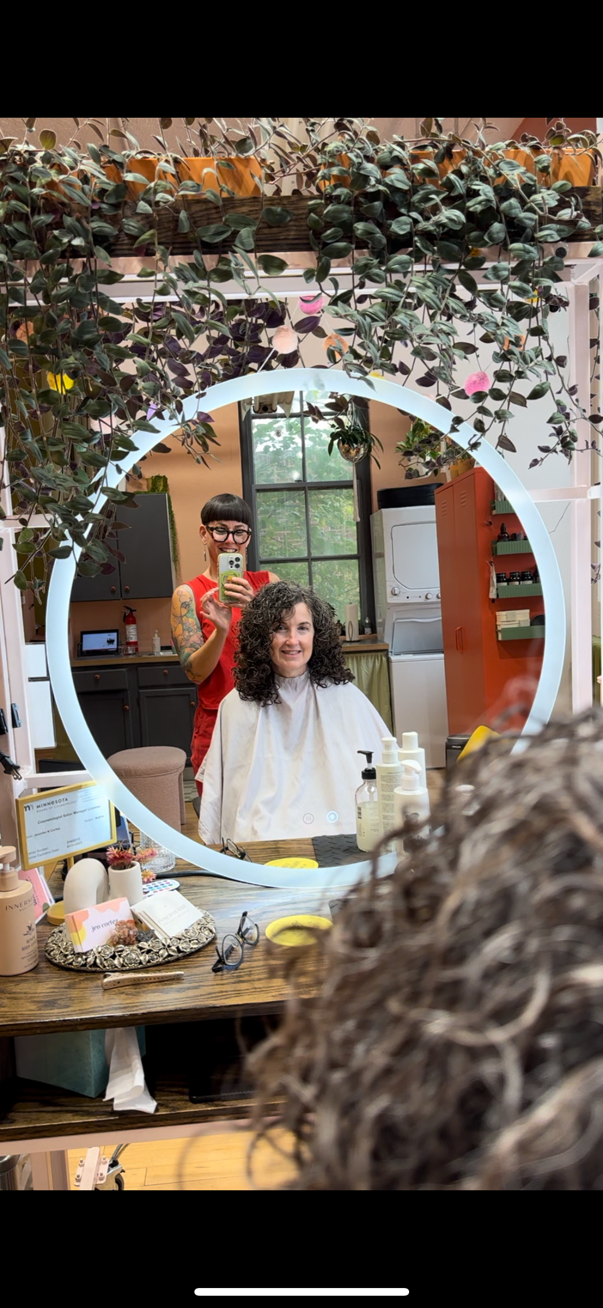 image of jen taking a POV  of a curly haircut she did, in the mirror with the client