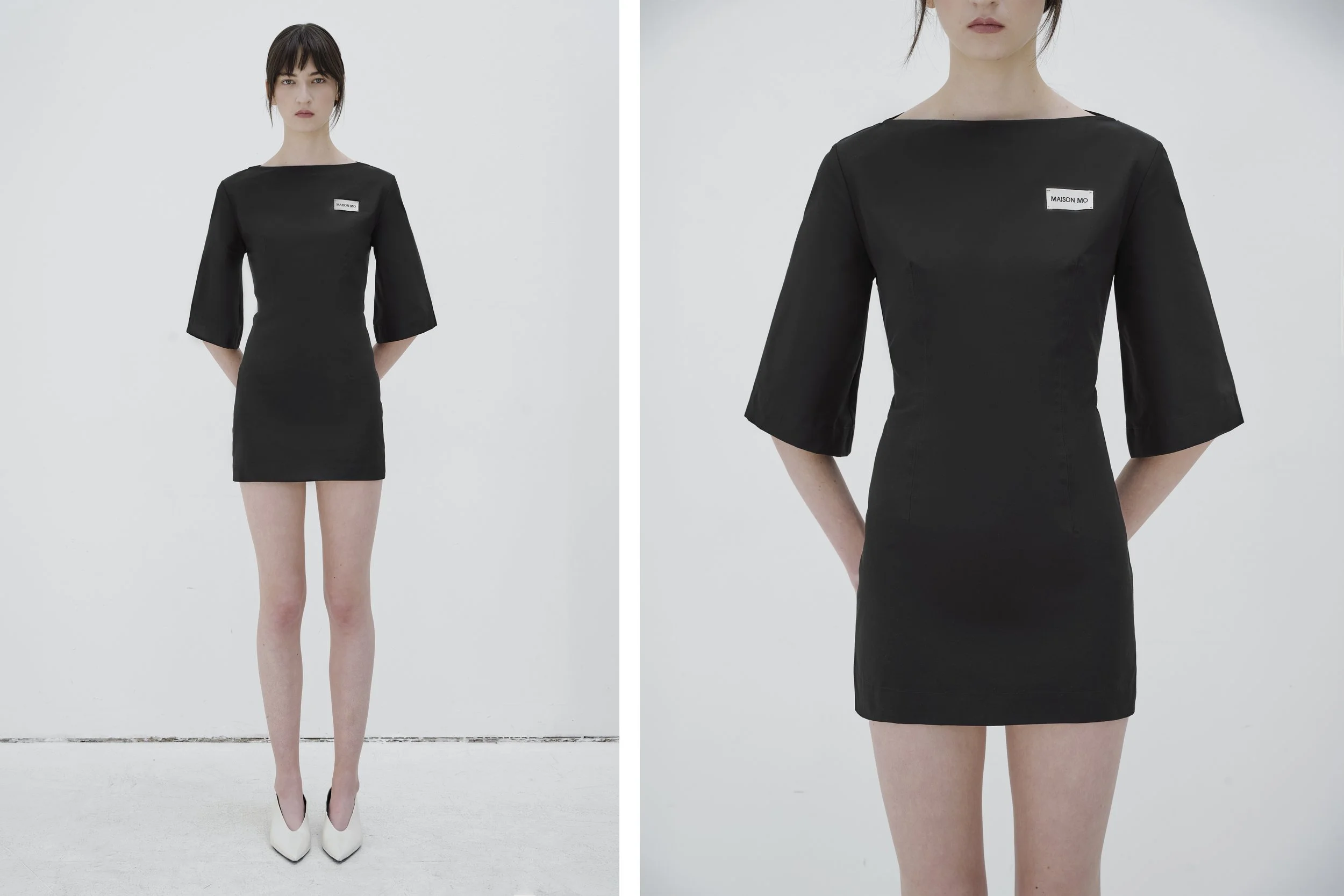Fashion photoshoot featuring a woman in a black dress with three-quarter sleeves and a small label on the chest, standing against a white background with white shoes.