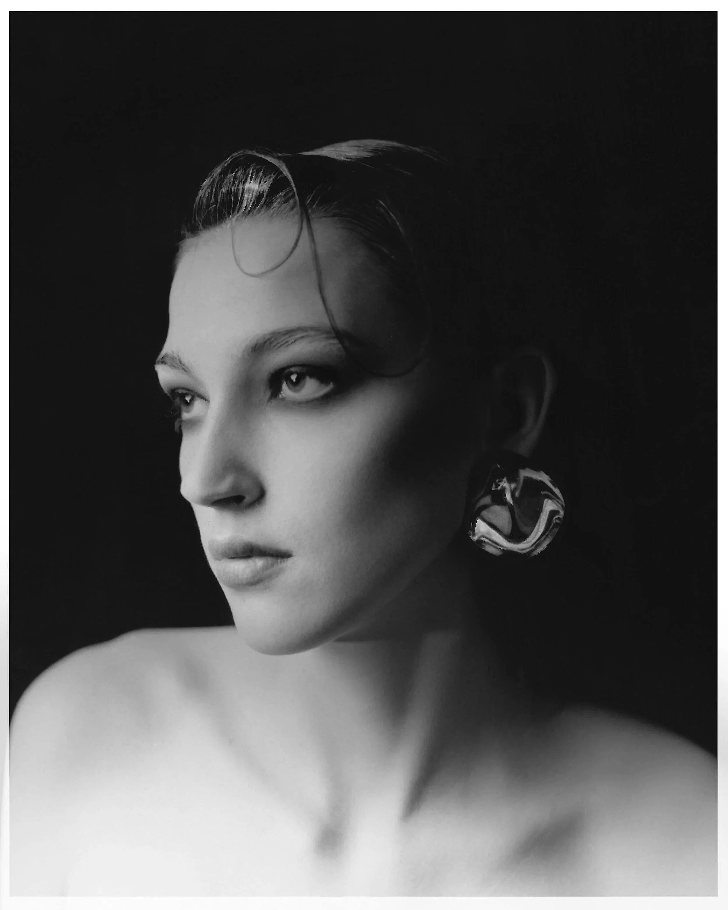 Black and white portrait of a woman with short, wet hair, wearing a large earring, looking to the side.