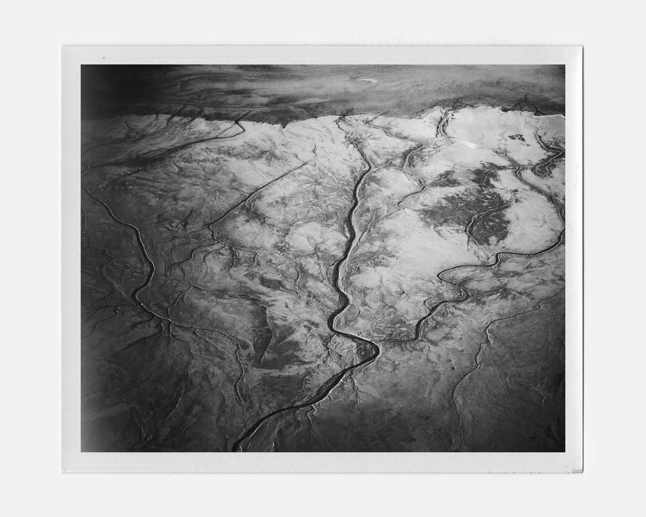 Black and white aerial photograph of a river system with multiple branching channels flowing through arid land, viewed from above.