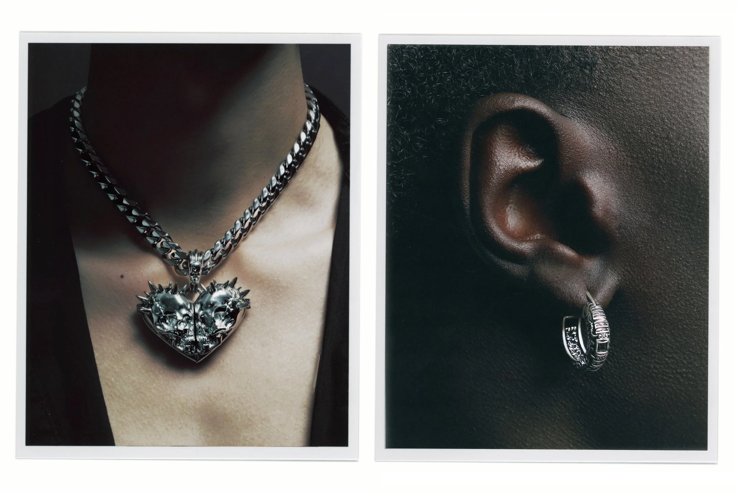 Close-up of a person wearing a thick silver chain necklace with a large, ornate heart-shaped pendant featuring spikes and skull motifs, and an ear adorned with a silver hoop earring engraved with text, against dark backgrounds.