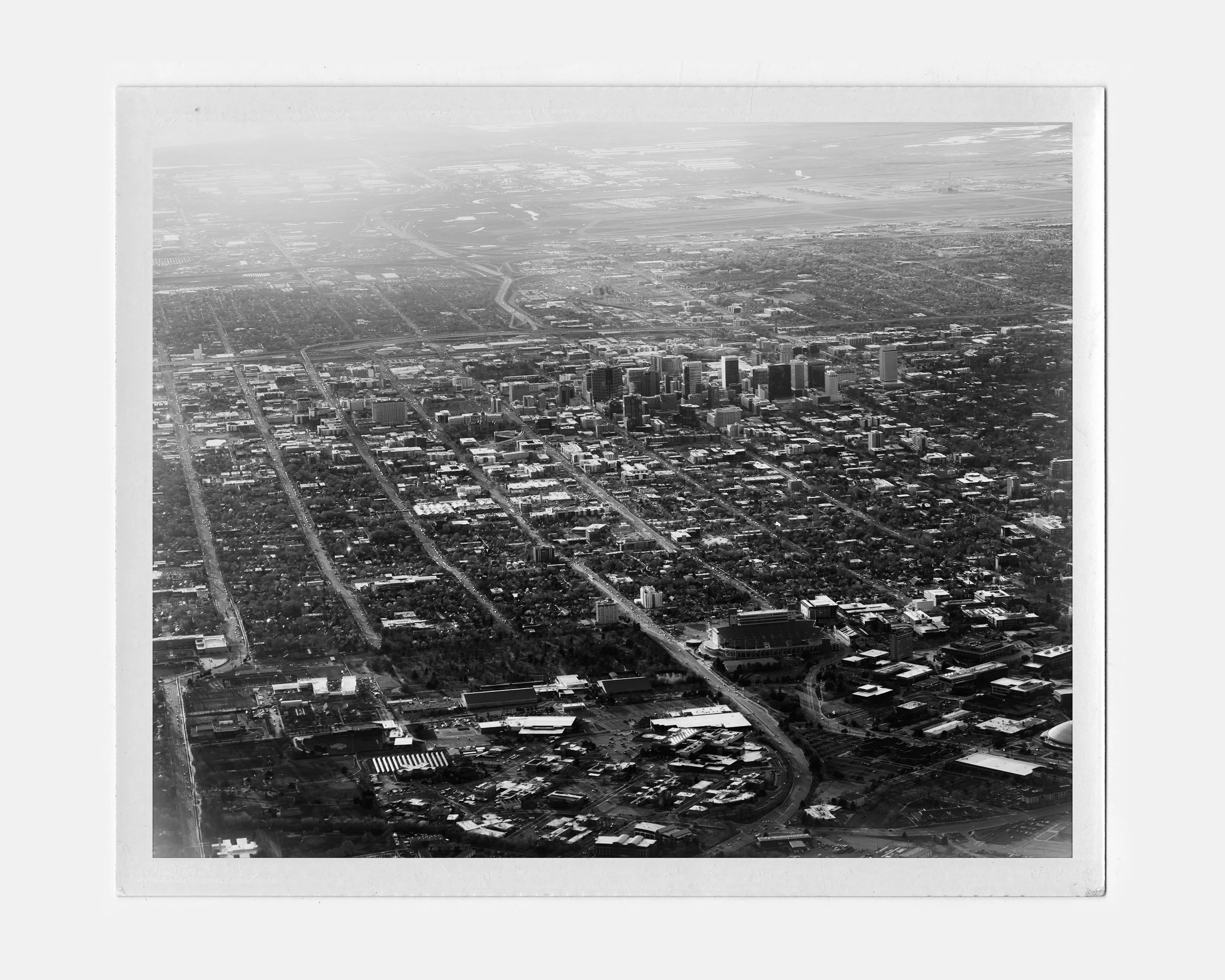 Black and white aerial photograph of a city skyline with tall buildings, streets, and surrounding urban area.