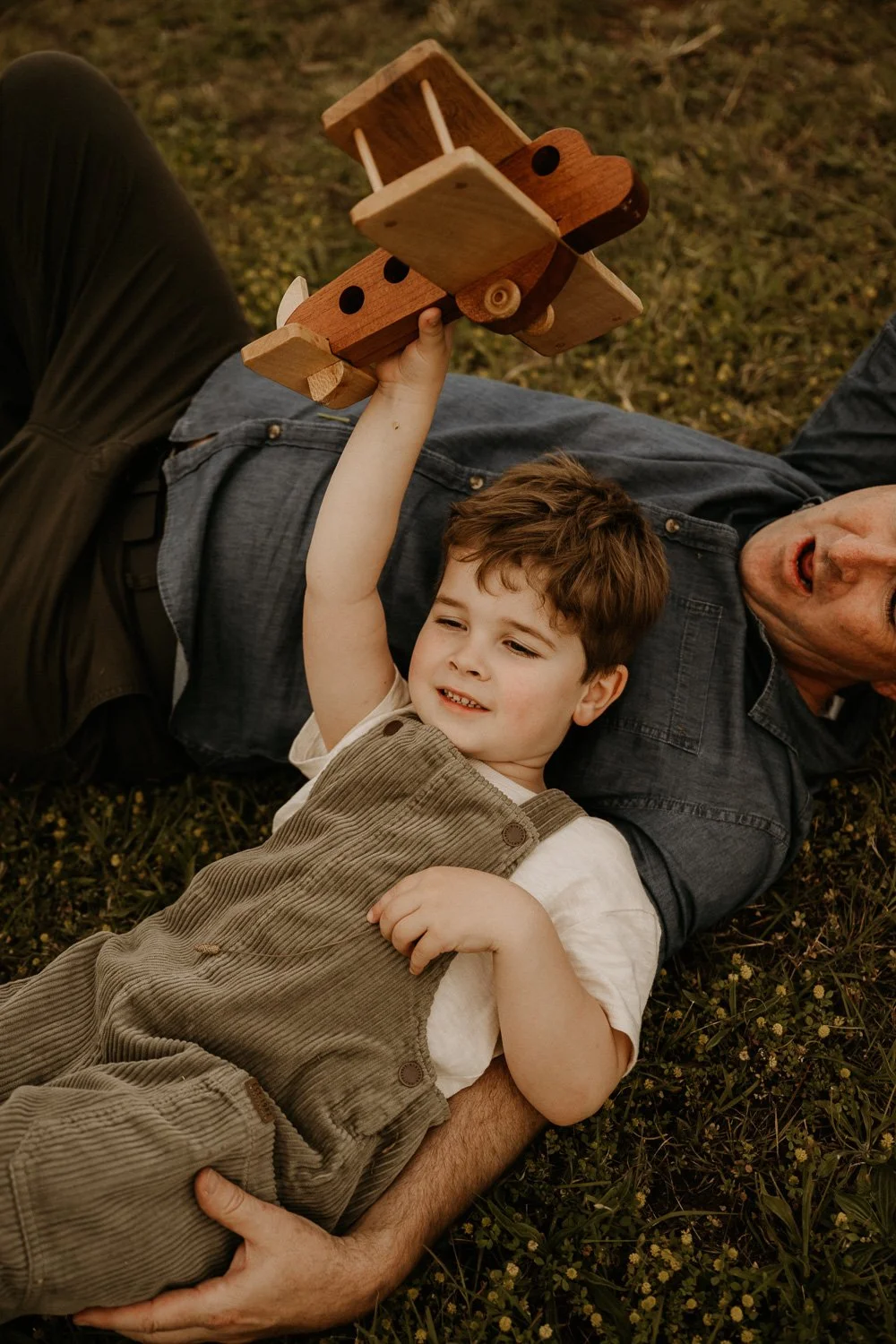 Young boy laying head on dad holding wooden aeroplane