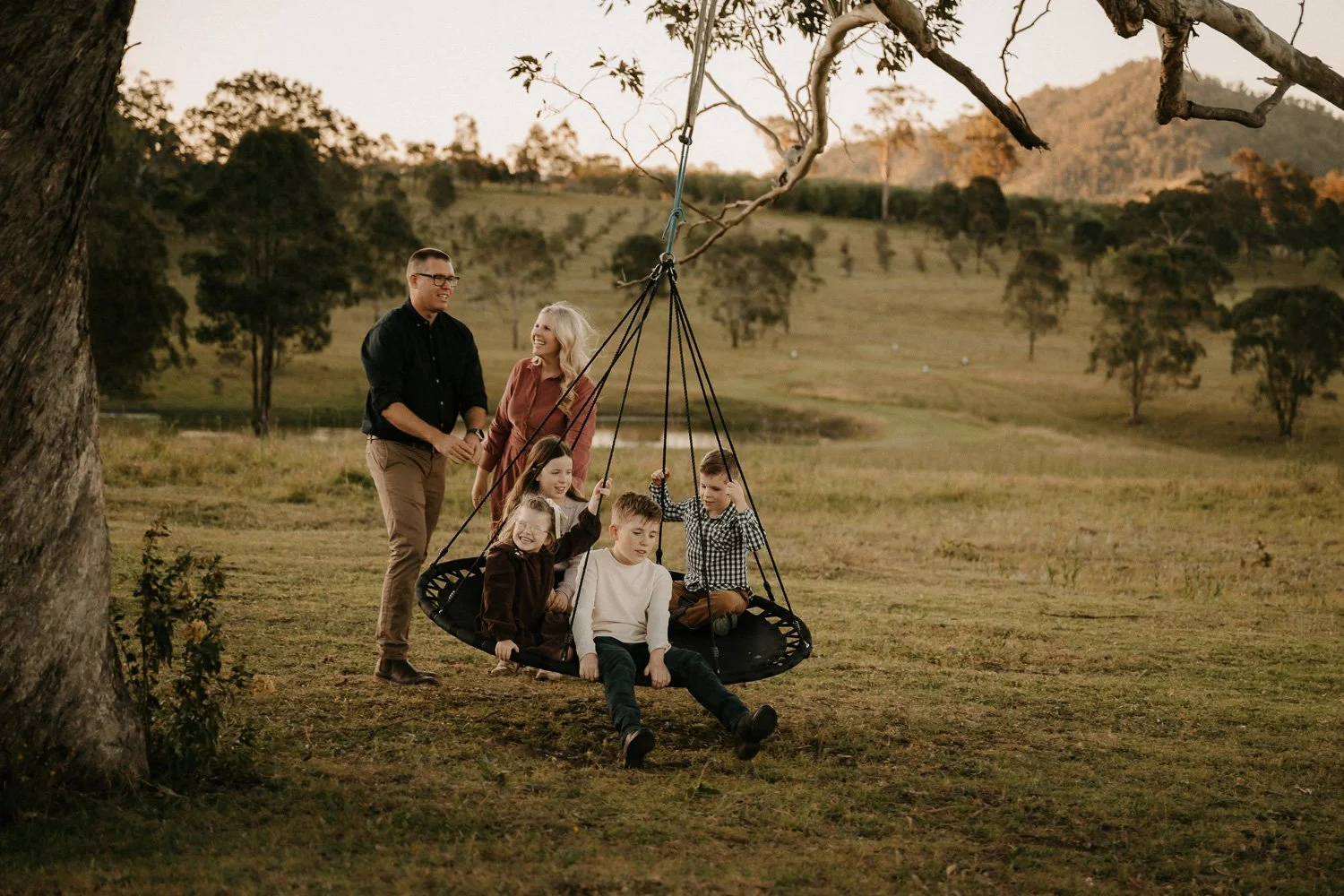 Kids being pushed on large swing on their property by dad while mum laughs at dad