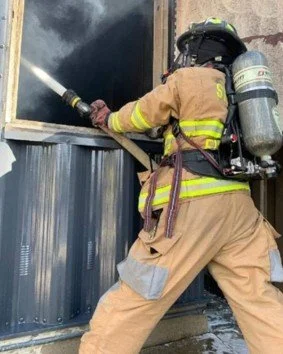 Firefighter spraying foam on the outside of a building during a fire rescue.