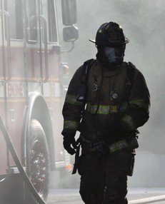 Firefighter in protective gear walking away from a fire truck