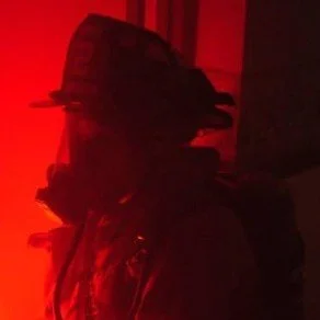 Silhouette of a person wearing a hat in a dimly lit red environment.