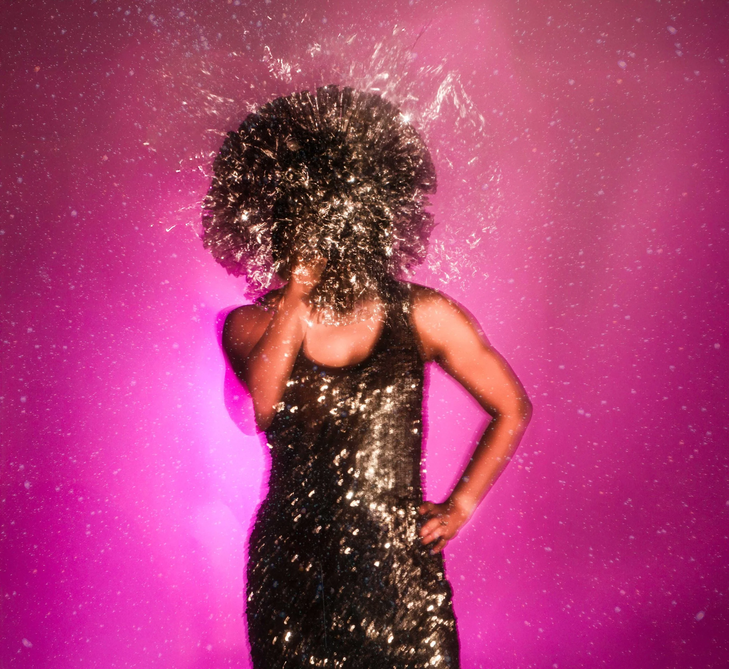 A woman in a black sequined dress is standing against a pink background, with her head resting on her hand. There are sparks or glitter around her head, creating a sparkling effect.