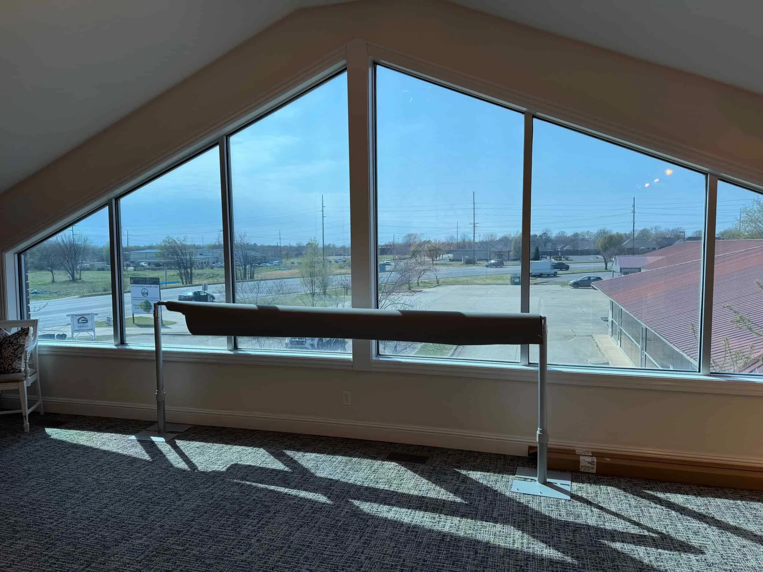 Interior view of a room with large triangular windows showing a parking lot and broad sky outside. Shadows cast on the patterned carpeted floor.