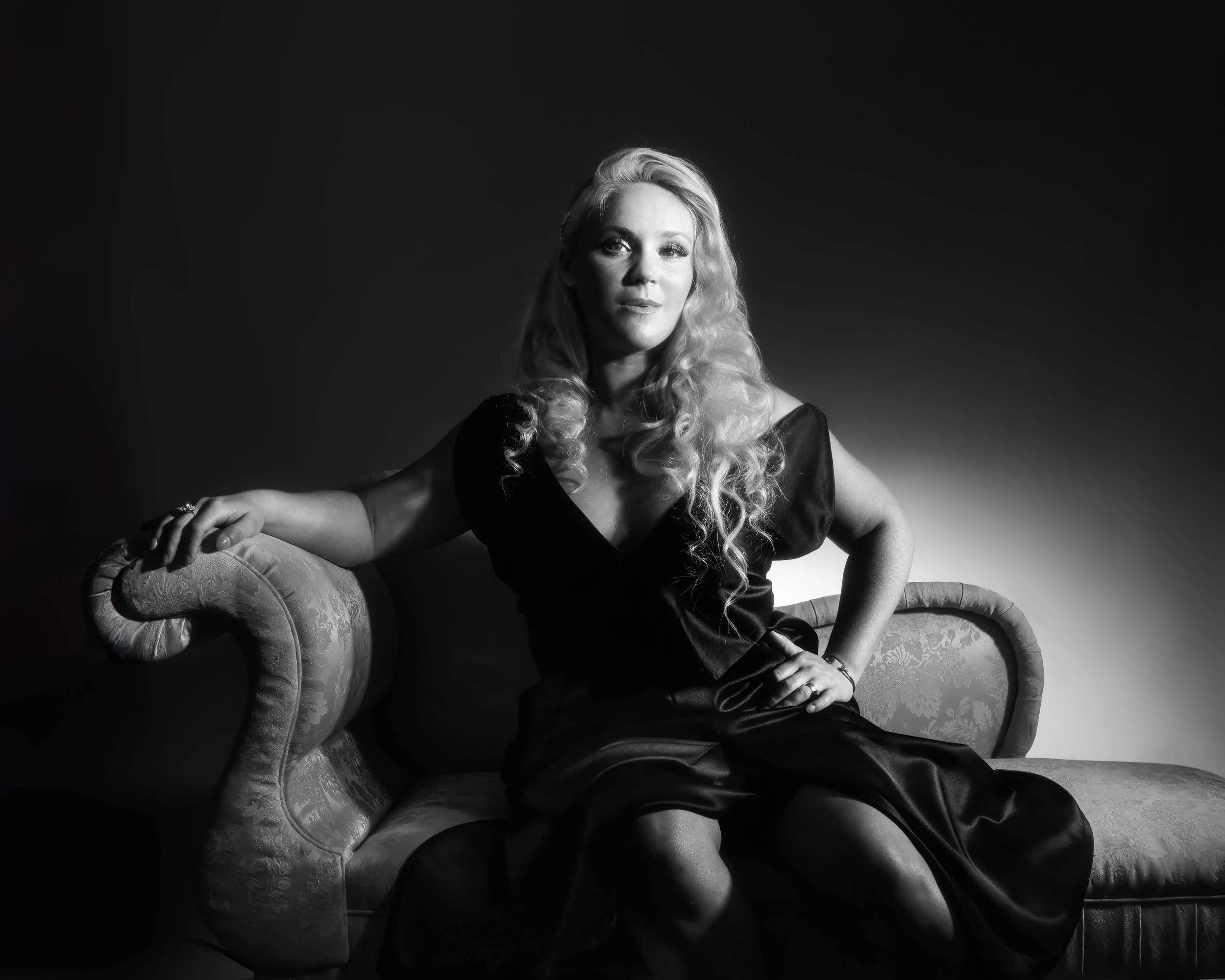 Woman posing on a chaise lounge in a black dress with dramatic lighting 