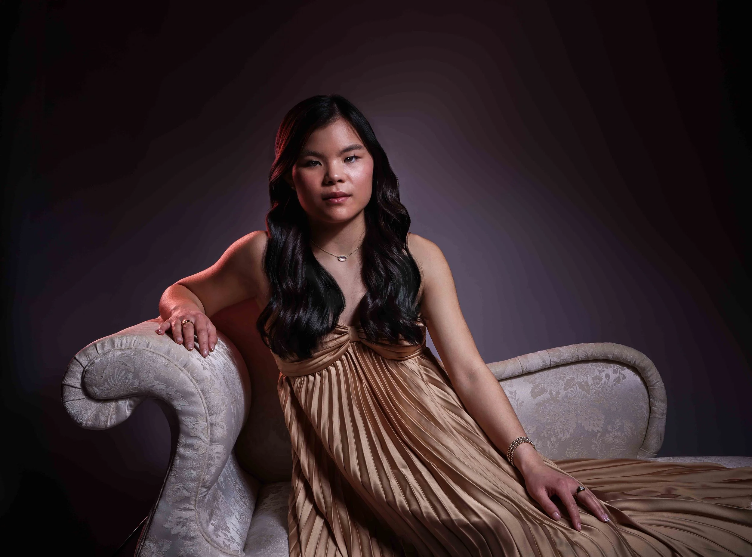 Studio portrait of a girl with black hair sitting on a chaise lounge
