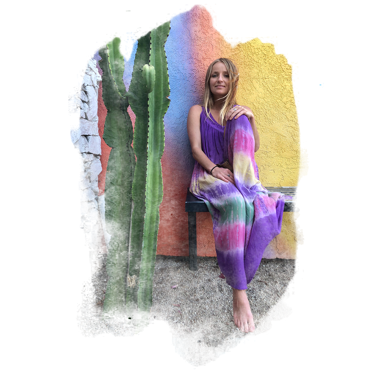 A woman with long blonde hair and a purple, pink, yellow, and green tie-dye dress sitting on a black bench next to a large cactus. She is barefoot and has her hand resting on her knee. Wild Chakra Kids founder kids mindfulness. Wild Goods.