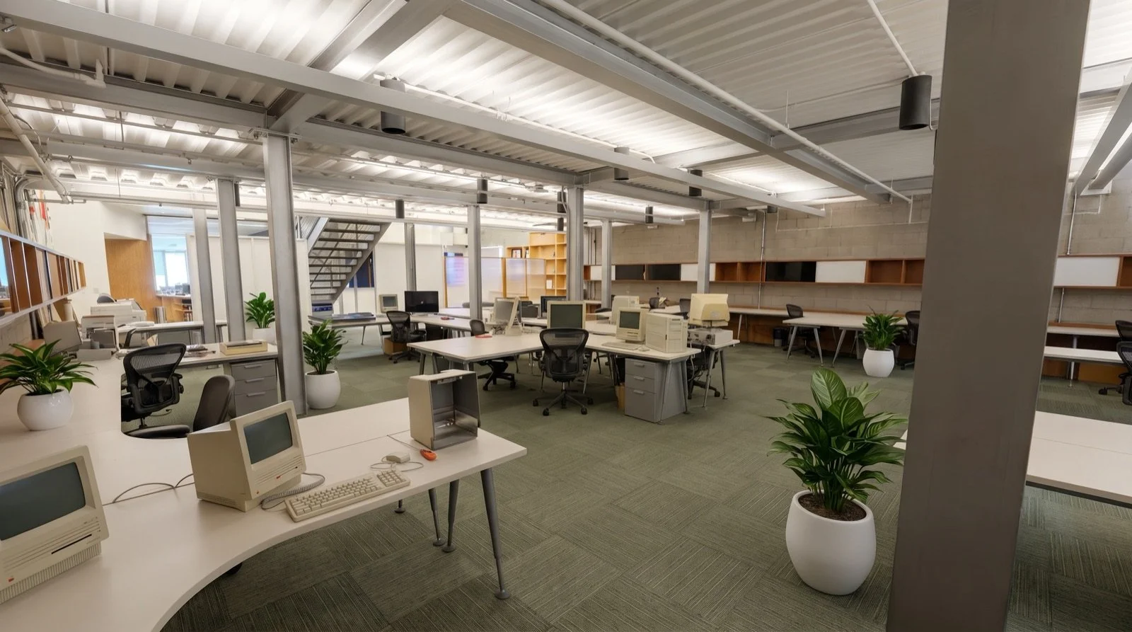 Empty modern office with desks, desktop computers, office chairs, and potted plants, with exposed ceiling and staircase in the background.