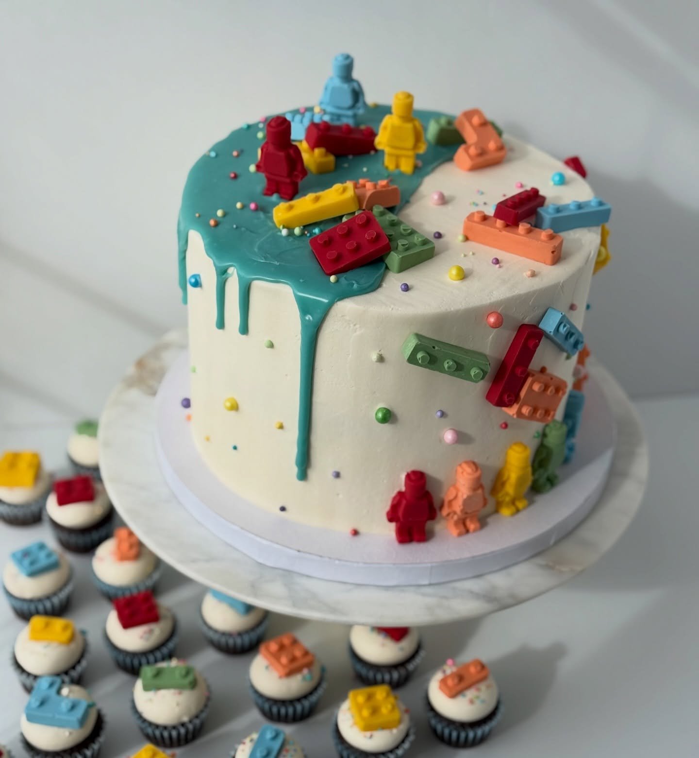 Lego Cake &amp; Cupcakes 

✨a best seller cake but with a new drip color 

✨this is one of my very faves designs , my fave part is the little LEGO people lined up around the cake base 

✨the Legos are made of dyed white chocolate that are molded in s