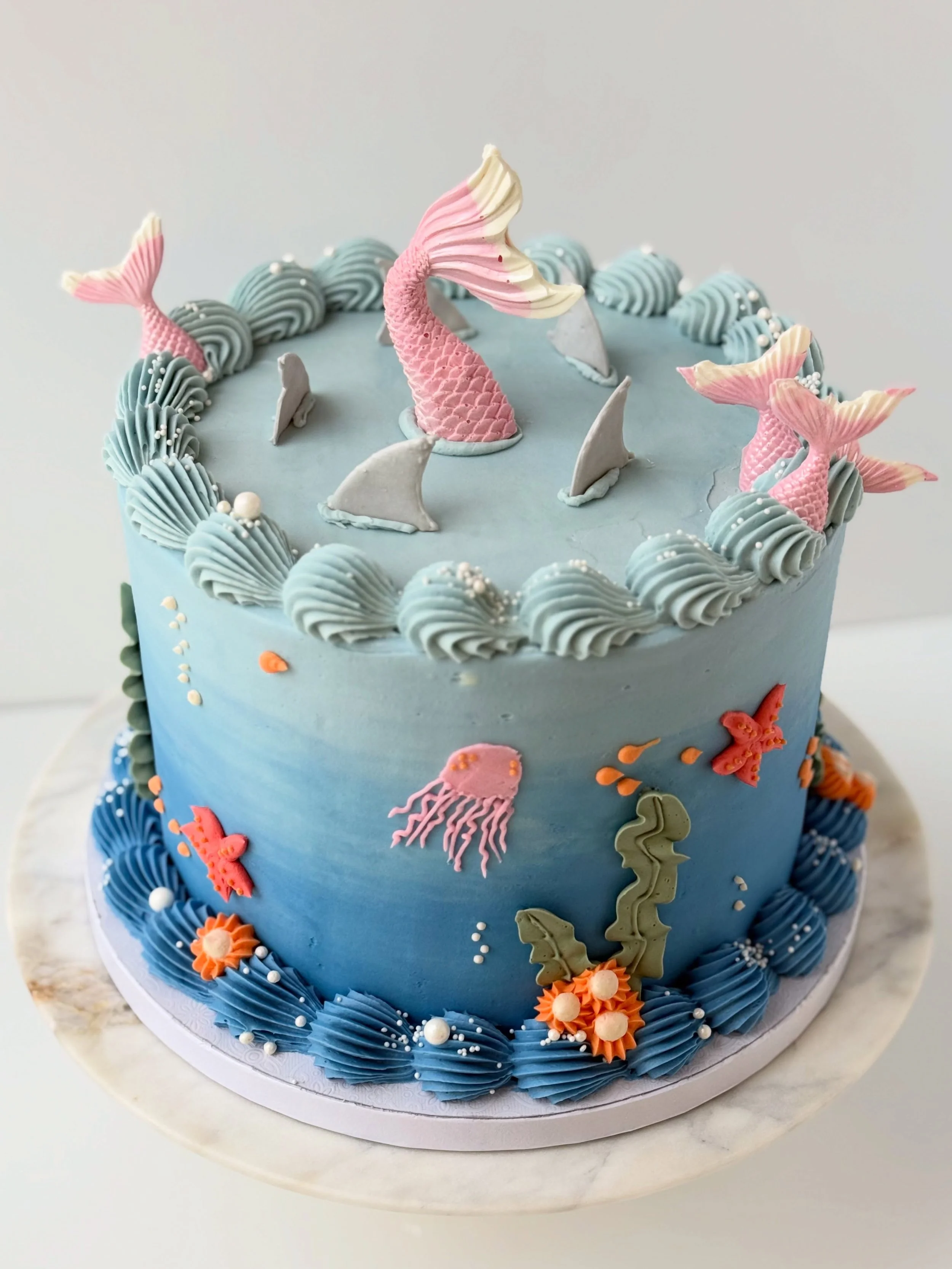 Under the Sea Cake 🧜🏻&zwj;♀️

✨I&rsquo;ve don&rsquo;t many under the sea cakes but this one has the most elements

✨for this cake I added royal icing shark fins &amp; white chocolate mermaid tails

✨every other element is buttercream 

Supplies @ny