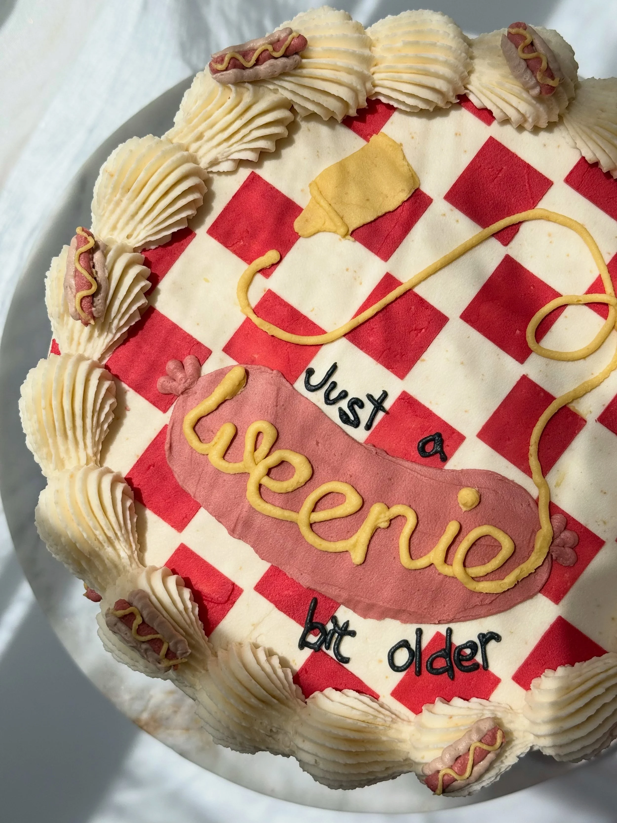 A weenie bit older 🌭

✨I&rsquo;m very over the tiny bit older cake trend but have been dying to do a weenie bit older!

✨complete with red checkered top &amp; piped mini hot dogs with the perfect mustard squiggle 

✨perfect for a Memorial Day weeken