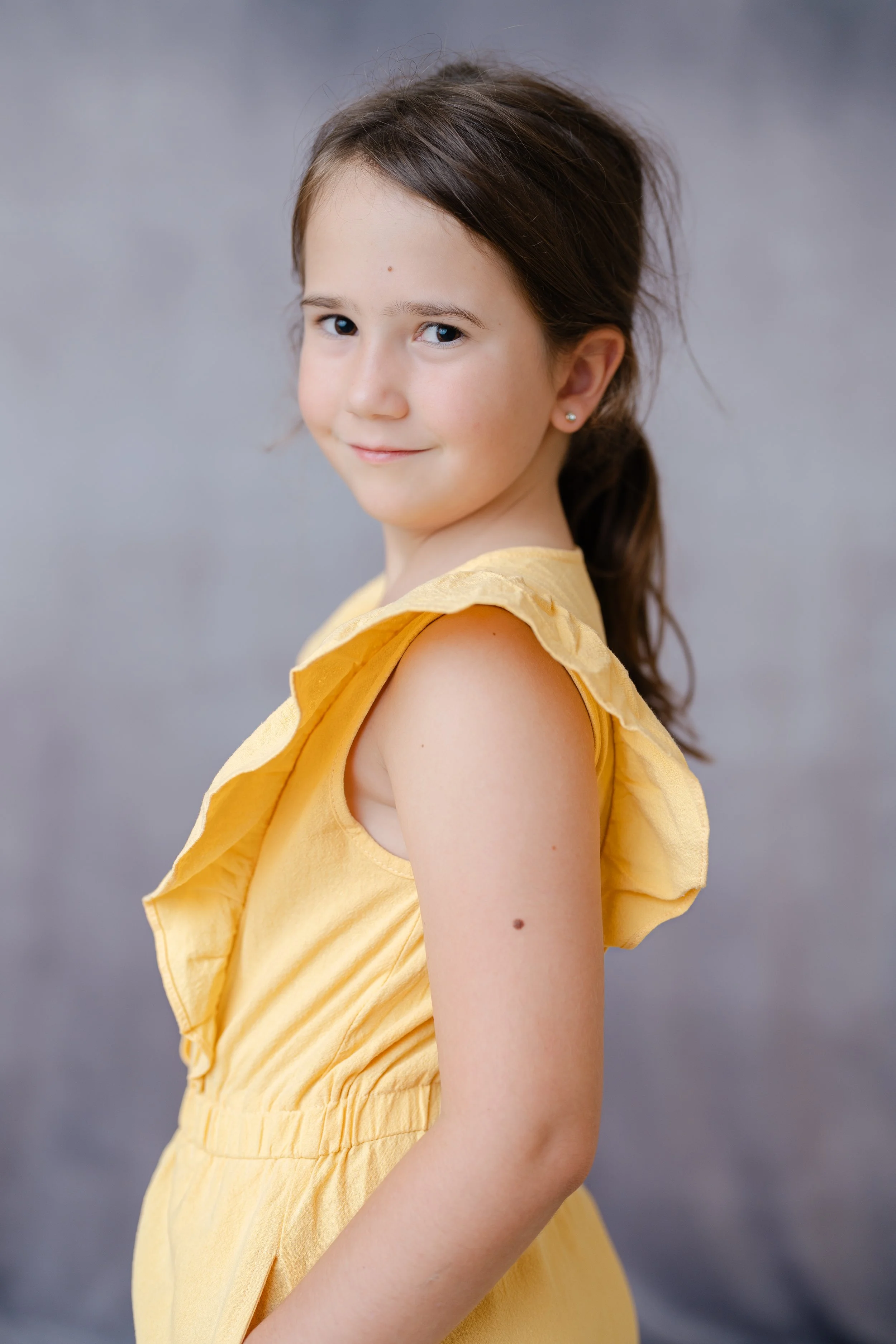 Portrait of a girl with a ponytail in a yellow ruffled dress, looking over her shoulder