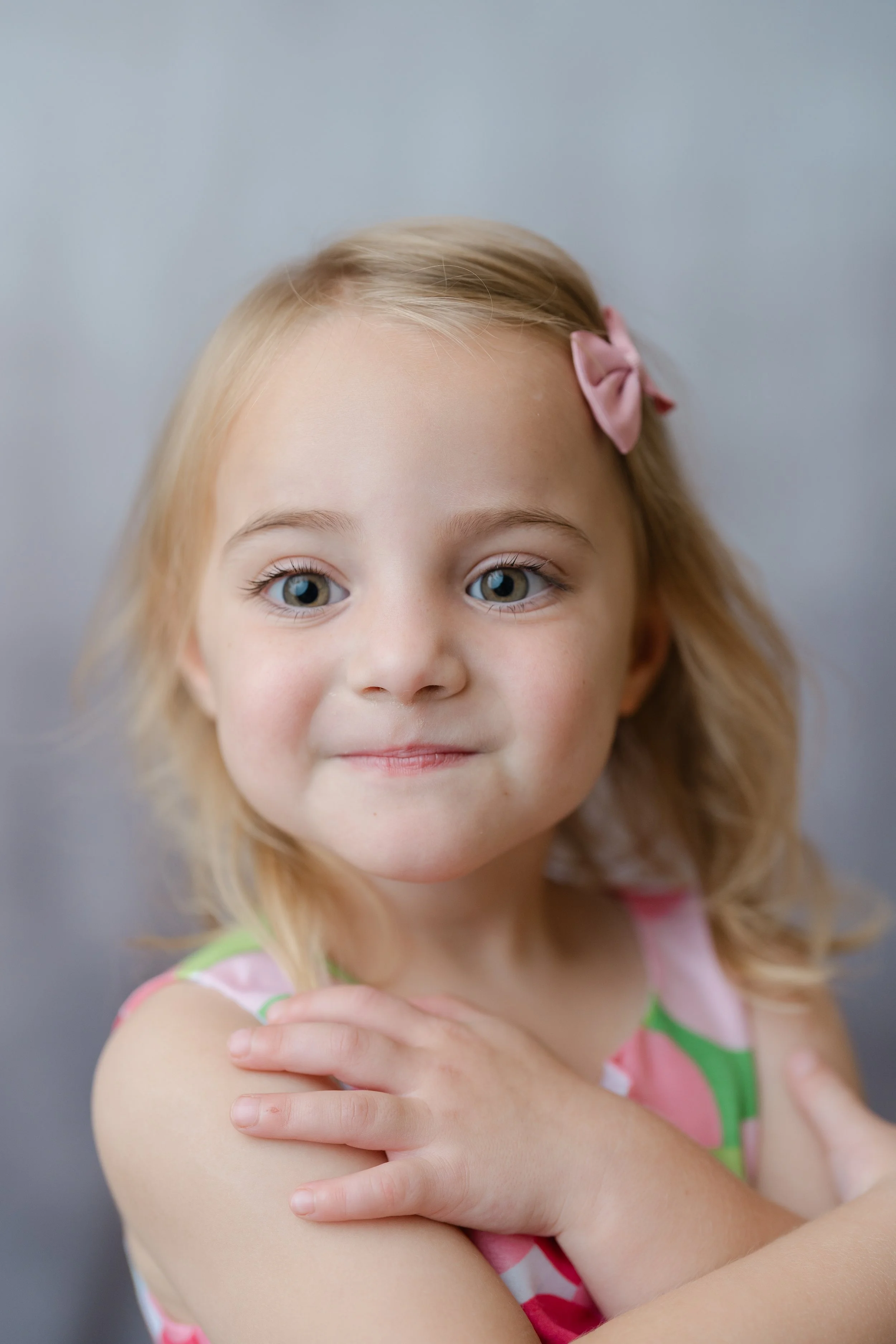 Portrait of a little girl with a pink bow, hugging her shoulders