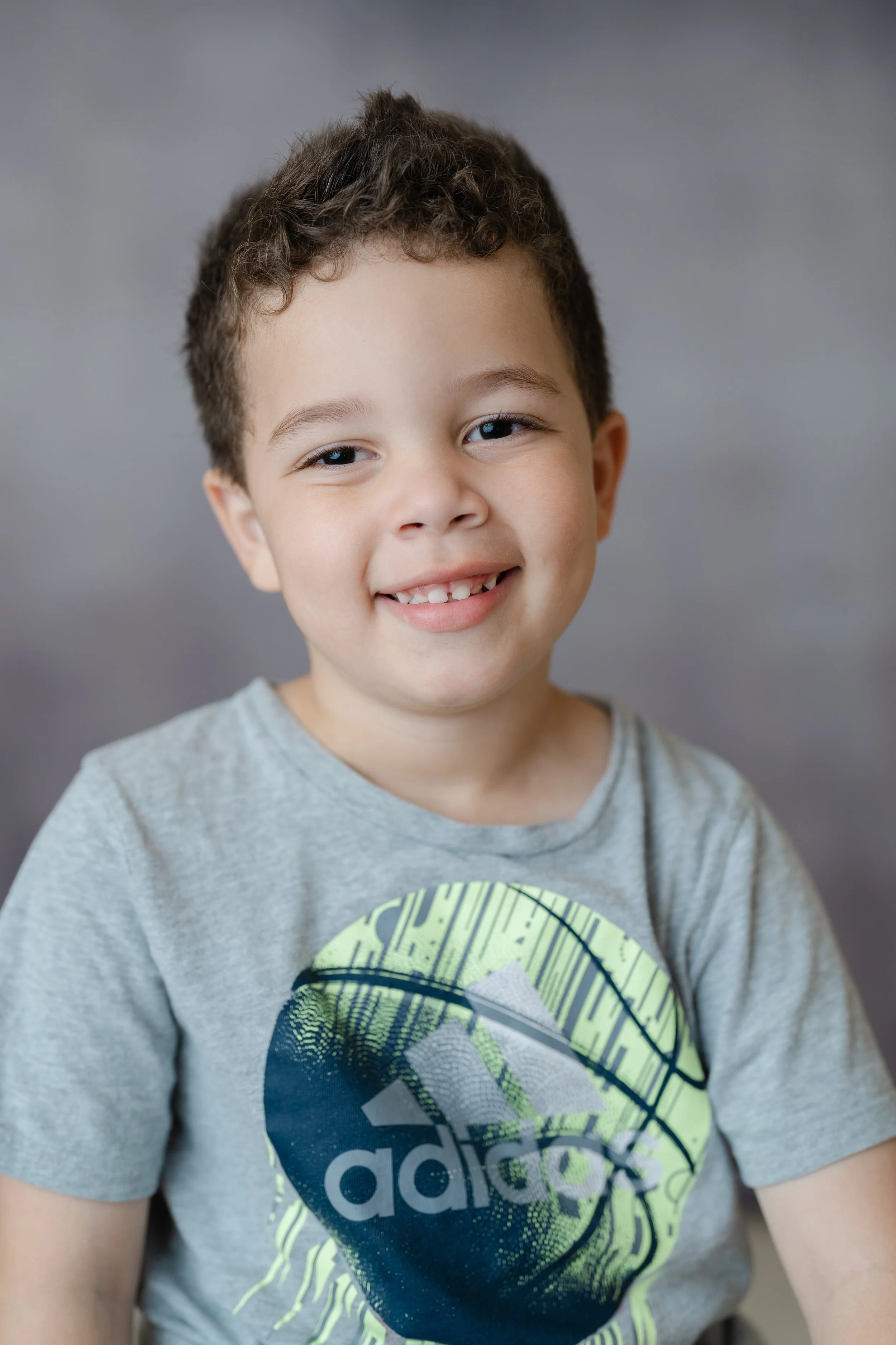 School portrait of a smiling boy with curly hair in a gray graphic T-shirt