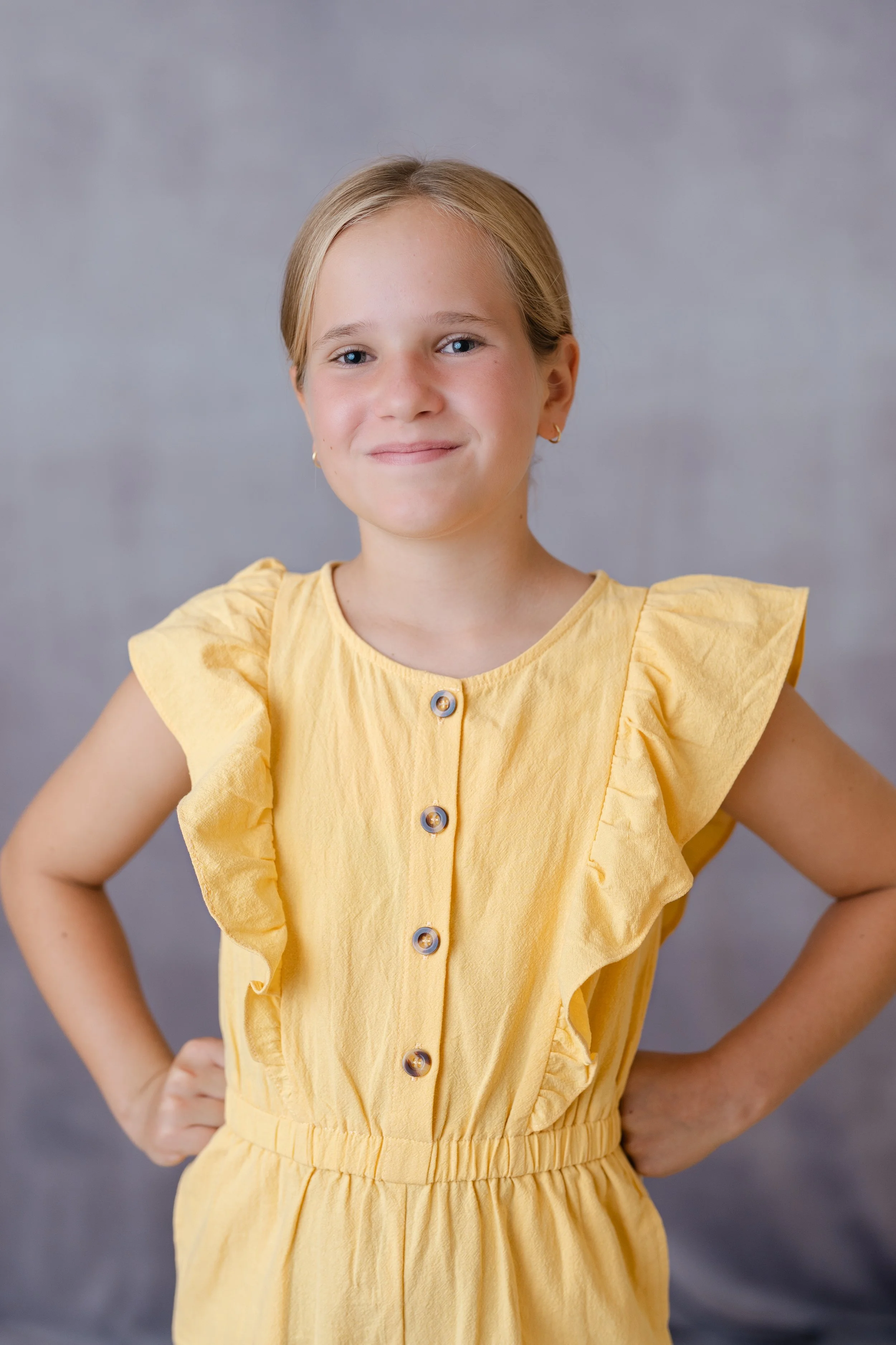 Portrait of a girl in a yellow ruffled dress with her hands on her hips