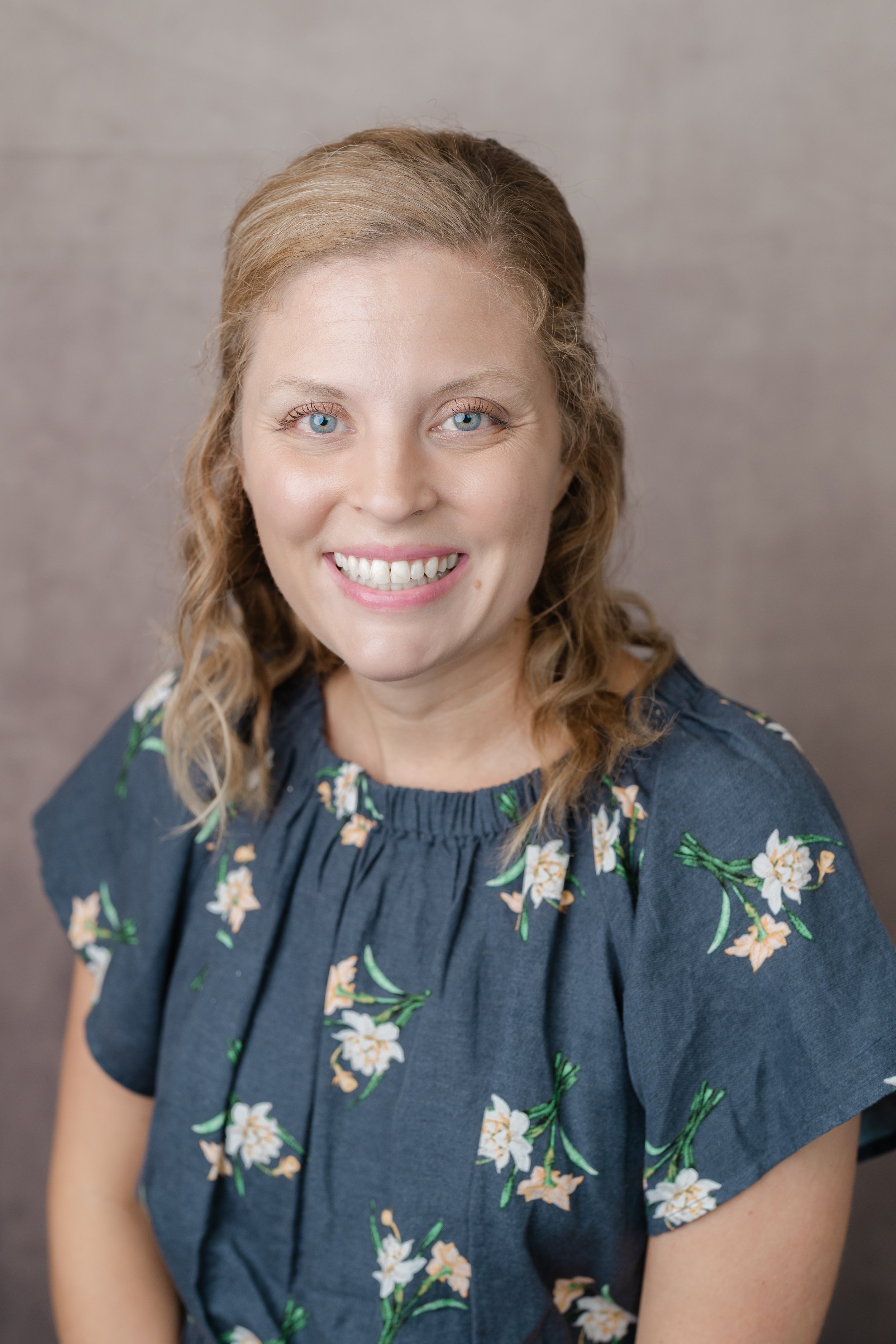 Professional headshot of a smiling woman with curly strawberry blonde hair in a navy floral blouse