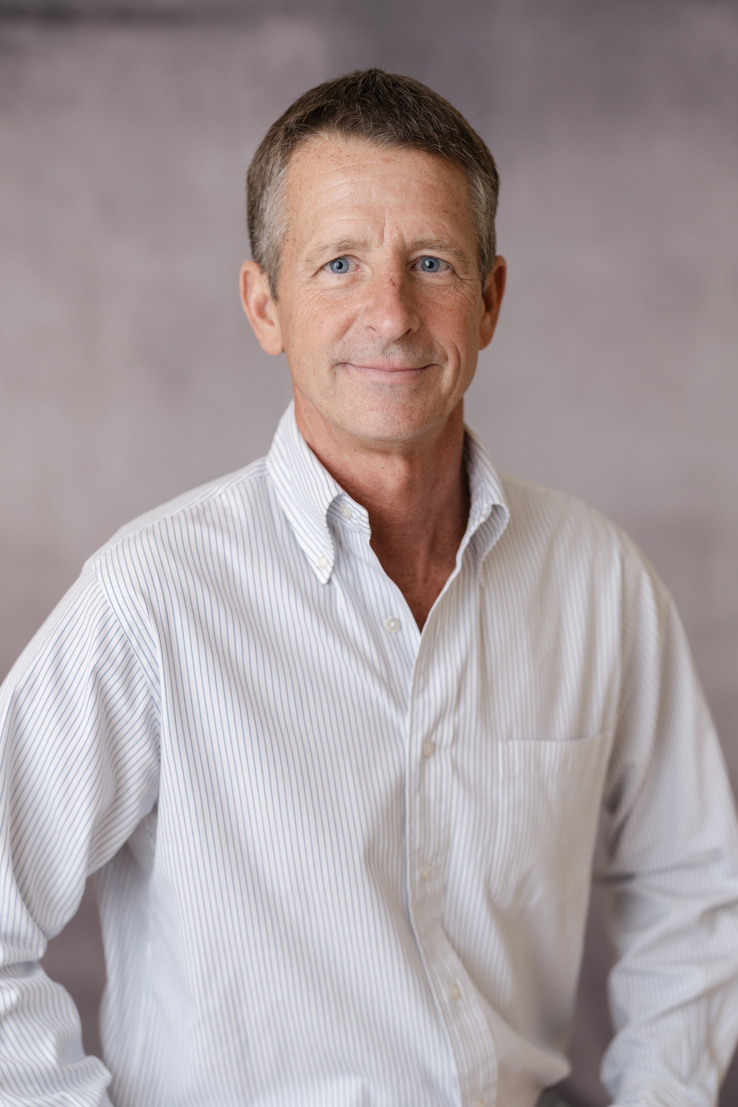 Professional headshot of a smiling man in a light button-down shirt