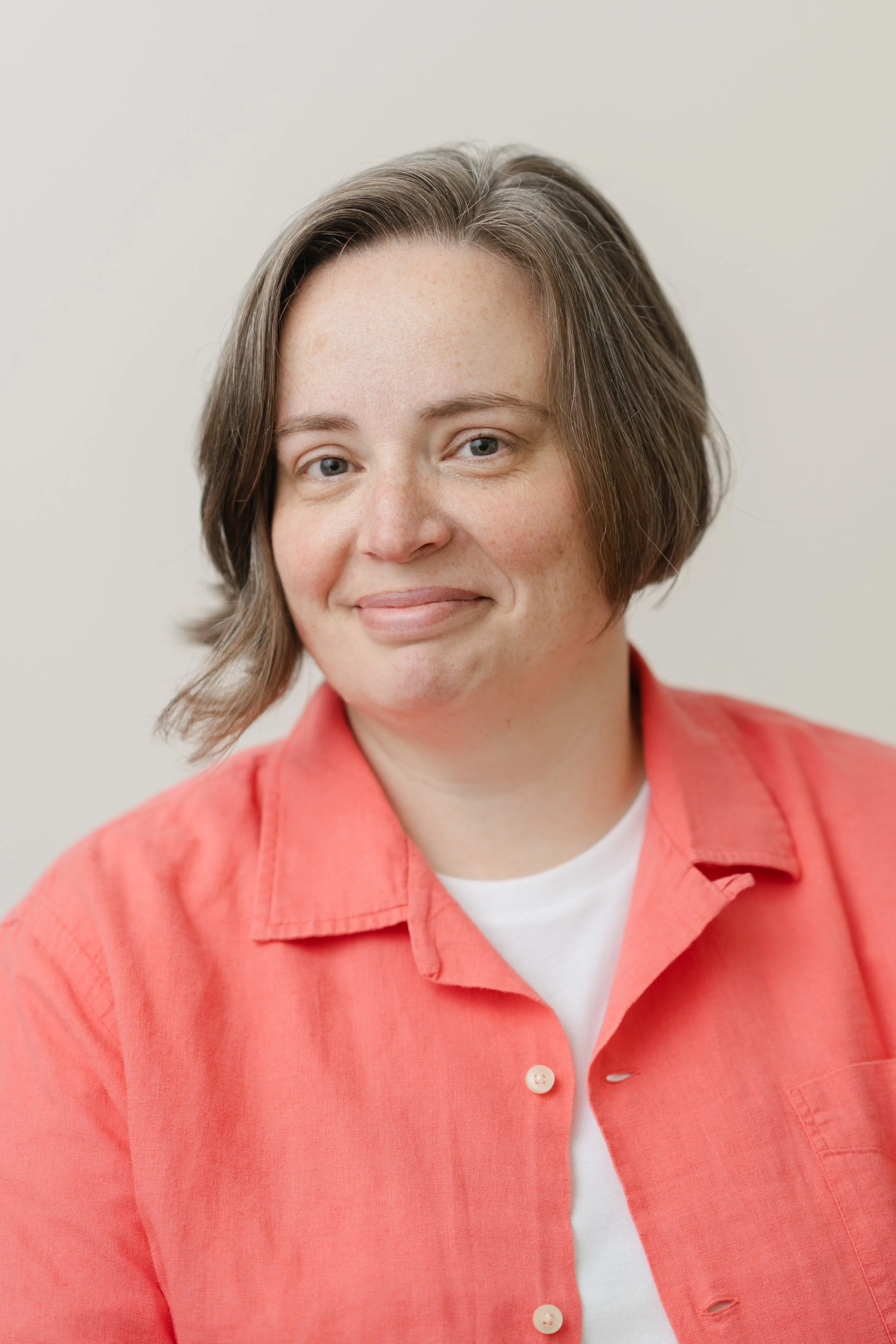 Professional headshot of a woman with short brown hair in a coral jacket