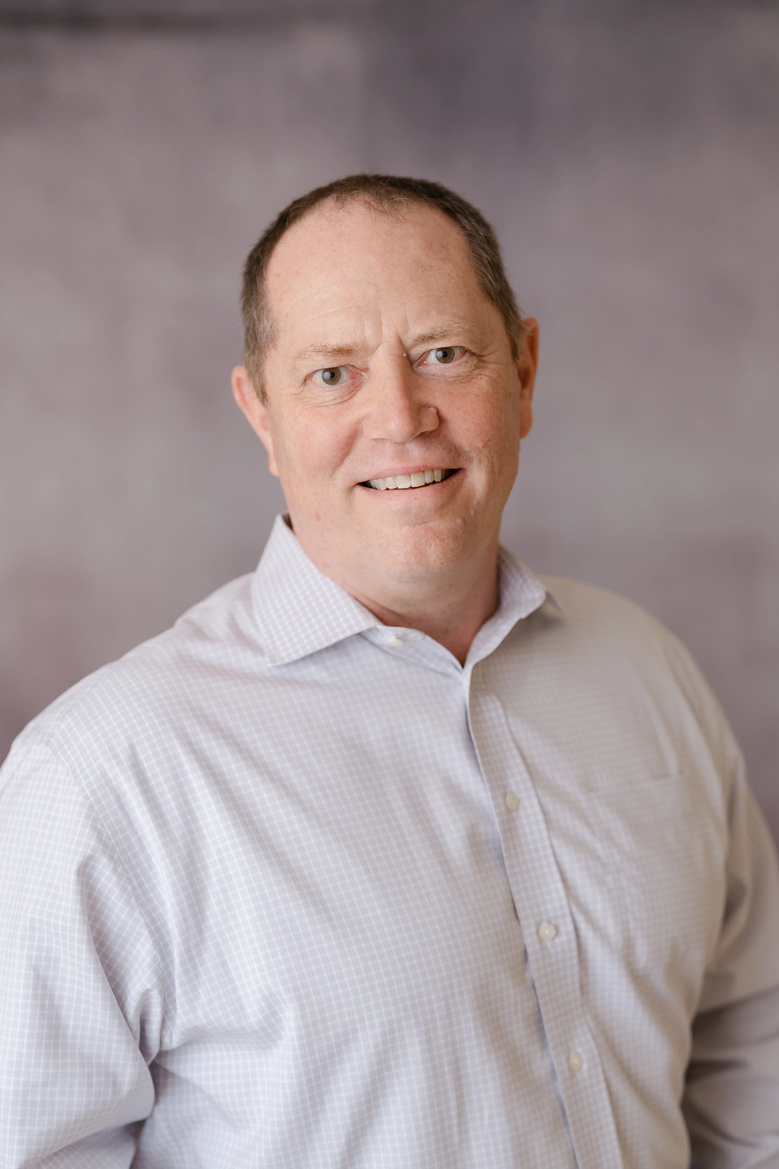 Professional headshot of a smiling man in a light pink button-down shirt