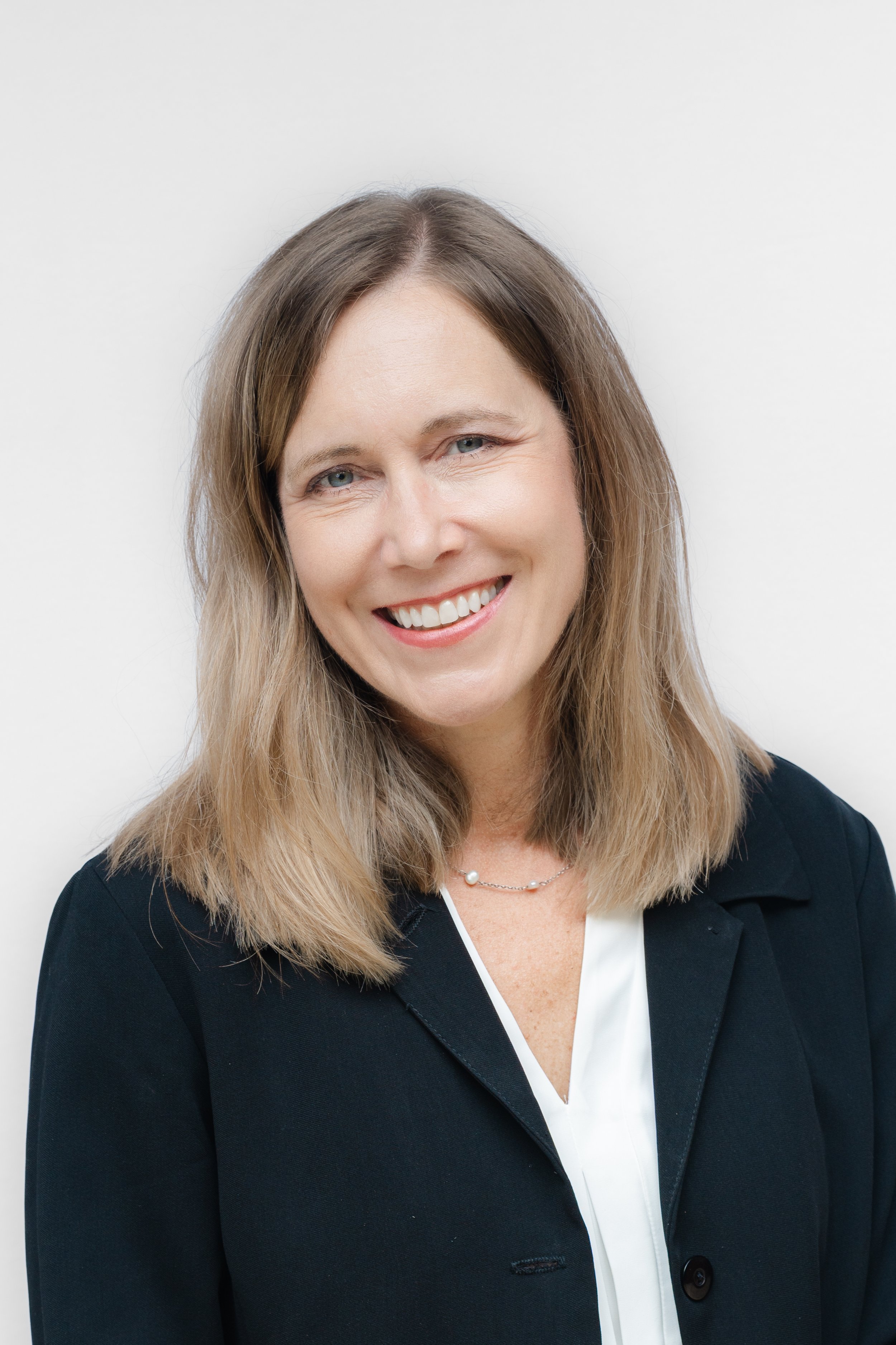 Professional headshot of a smiling woman with shoulder-length brown hair in a black blazer