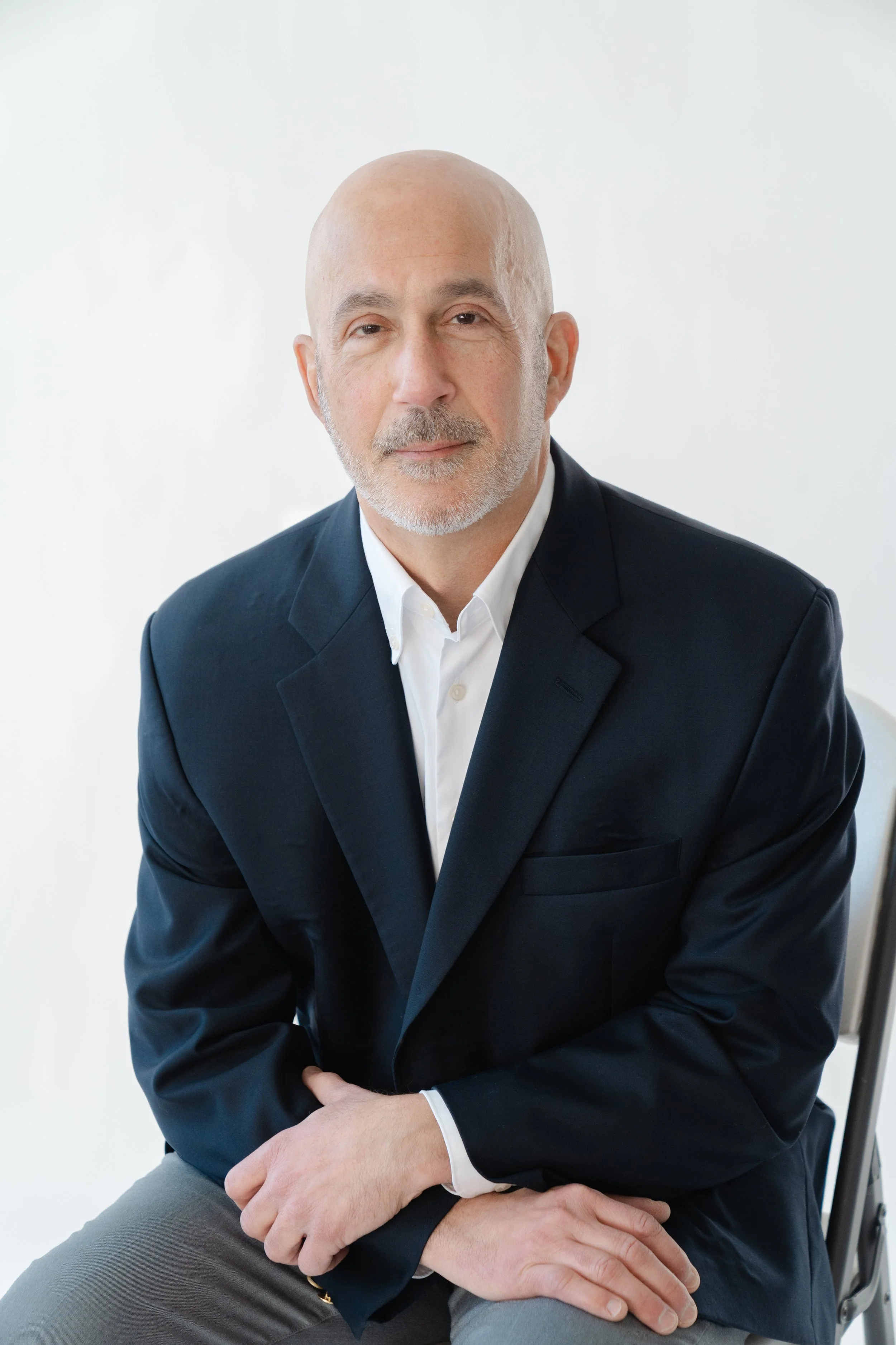 Professional portrait of a man in a navy blazer, seated against a light background
