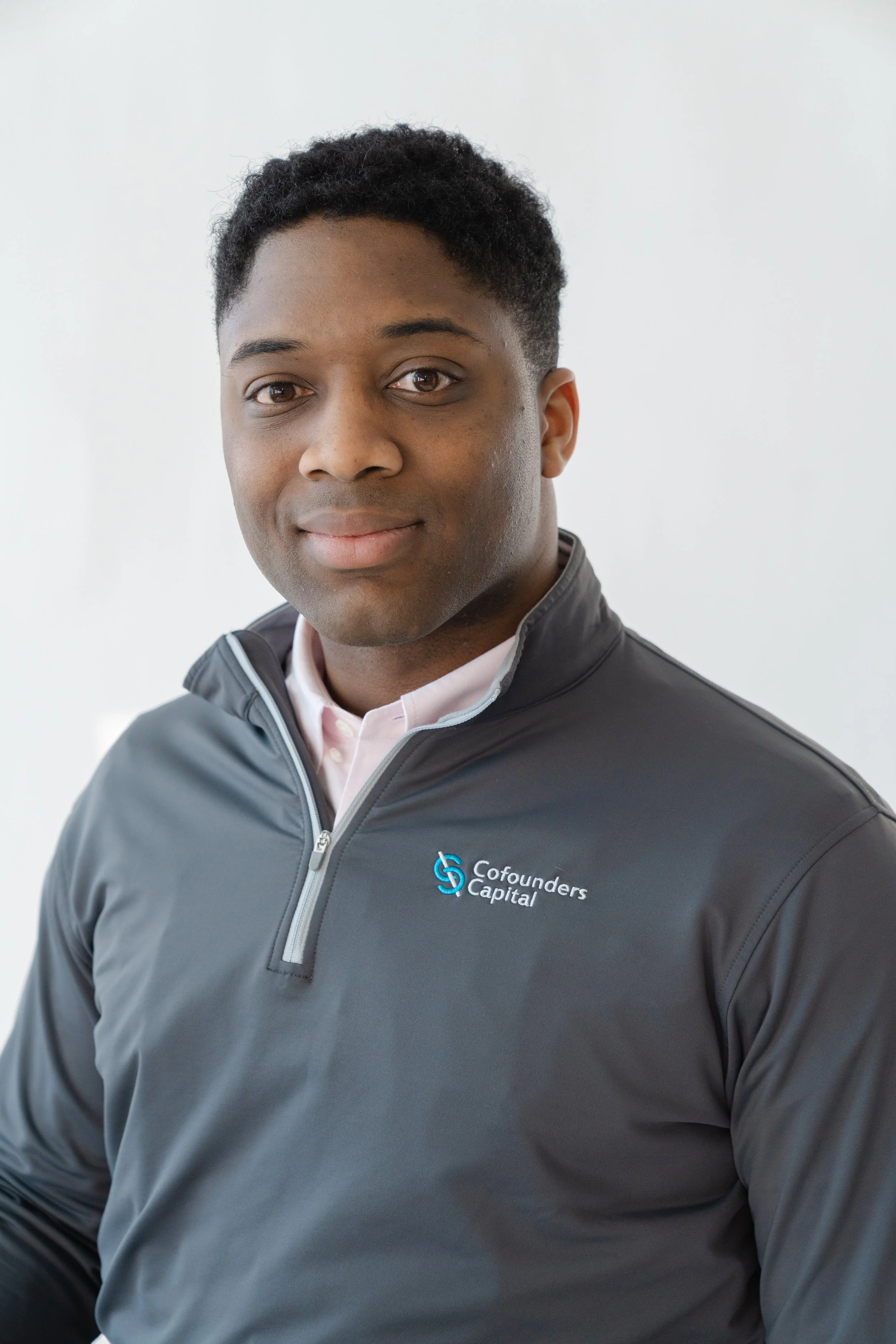 Professional headshot of a smiling young man in a gray quarter-zip pullover