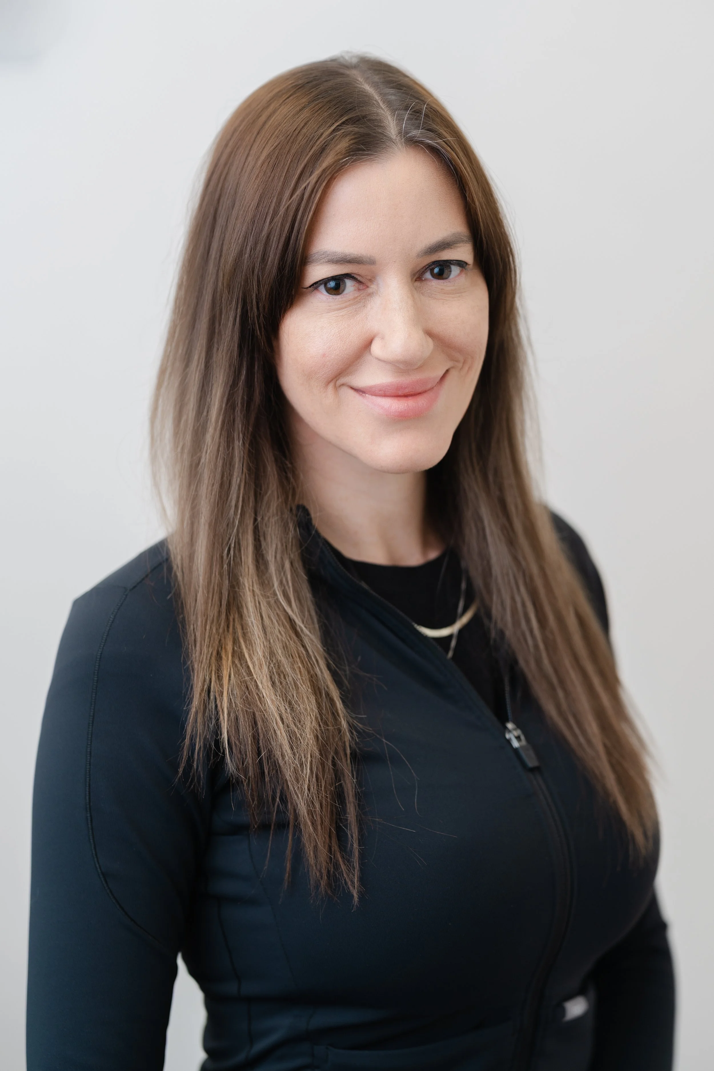 Professional headshot of a woman with long brown hair and a pendant necklace in a black top
