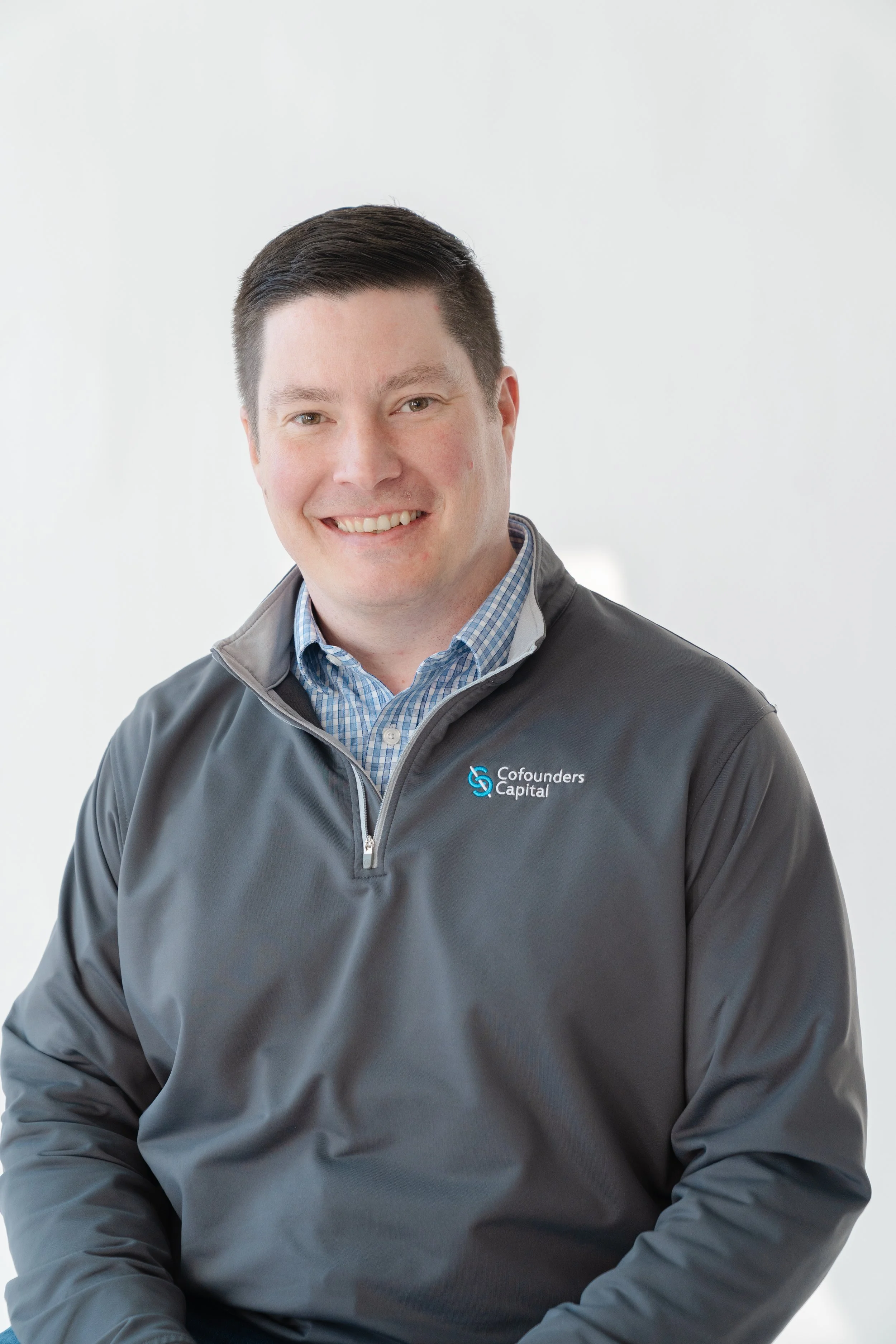 Professional headshot of a smiling man in a gray quarter-zip pullover